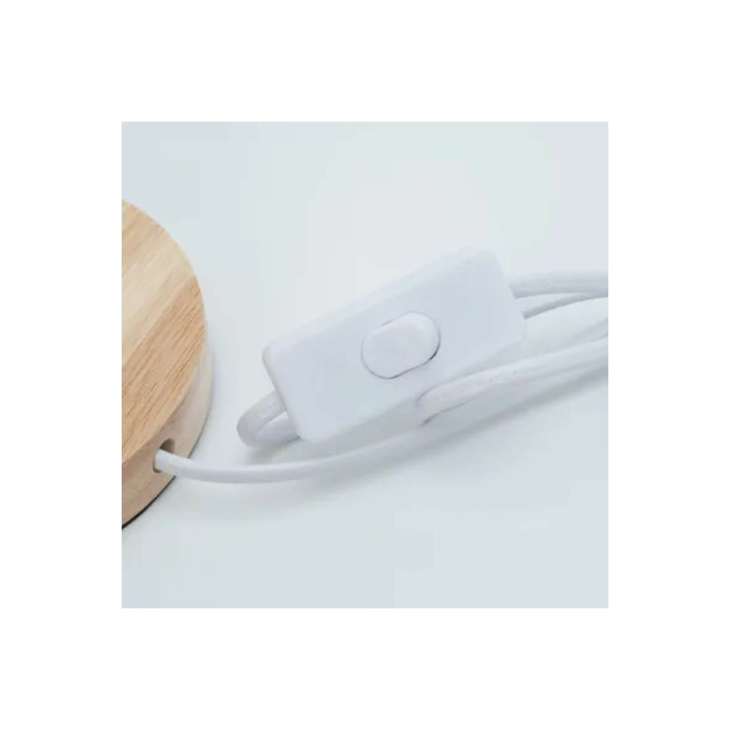 Ein weißer Lichtschalter an einem weißen Elektrokabel, das mit einem Holzsockel verbunden ist.