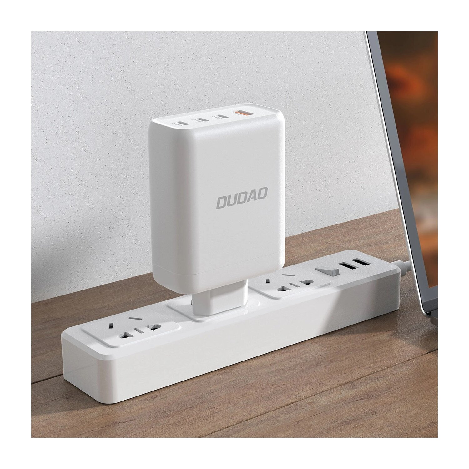 Ein weißer DUDAO-Netzadapter, der an eine Steckdosenleiste angeschlossen ist, zusammen mit einem Laptop auf einer Holzoberfläche.