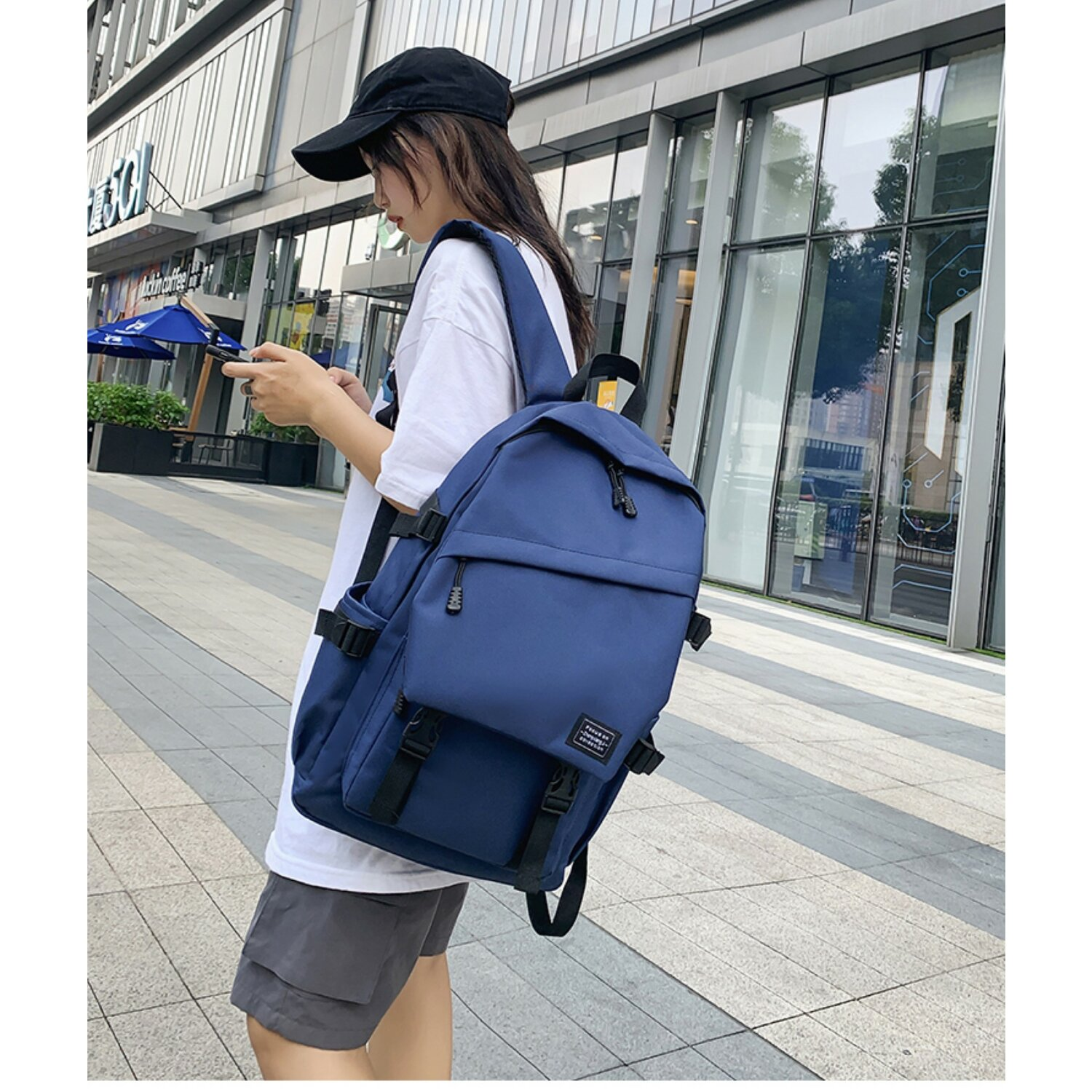 Frau mit blauem Rucksack geht auf einer Stadtstraße, hält ihr Telefon.