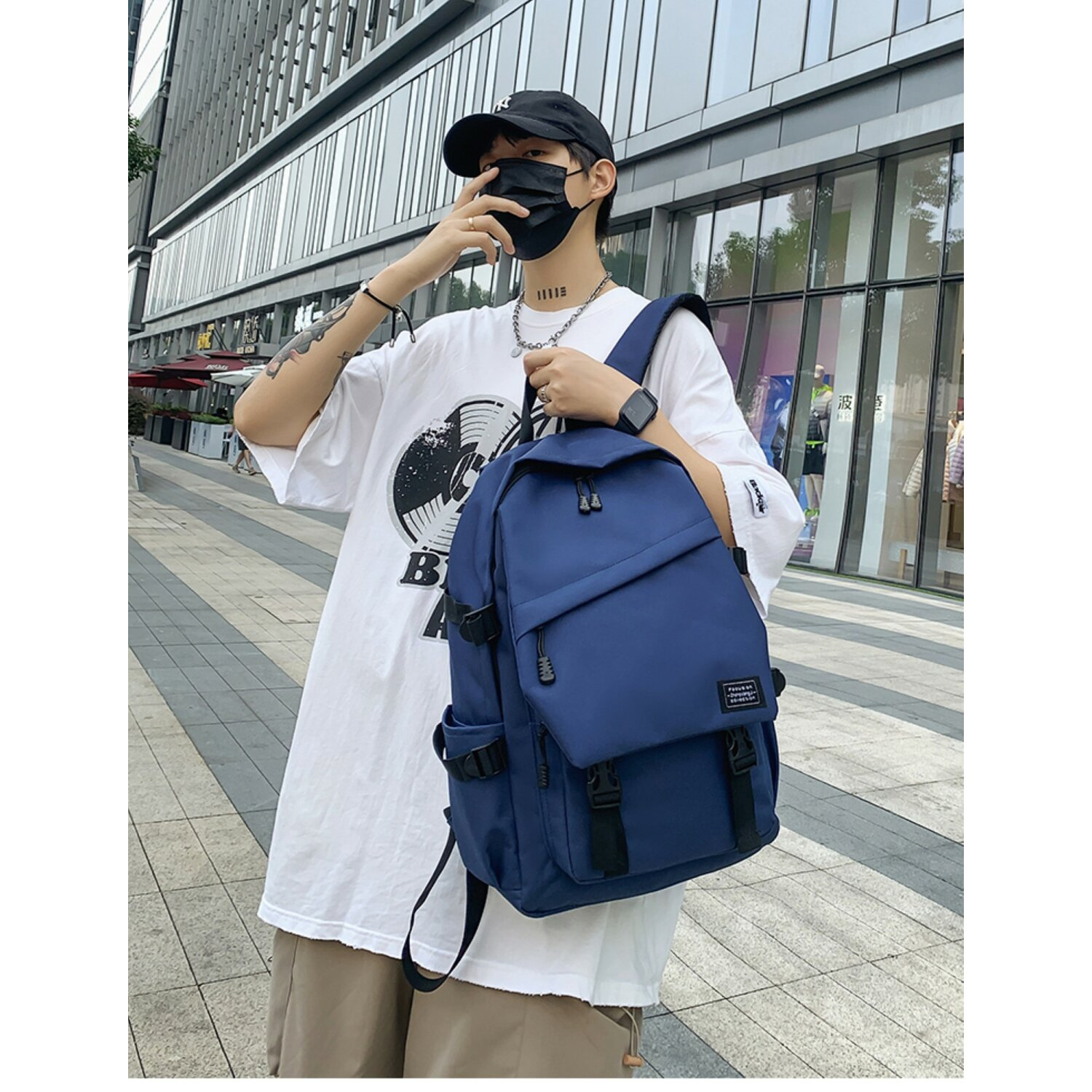 Mann in weißem T-Shirt, schwarzer Maske und Rucksack. Draußen gehen, Gebäudehintergrund.