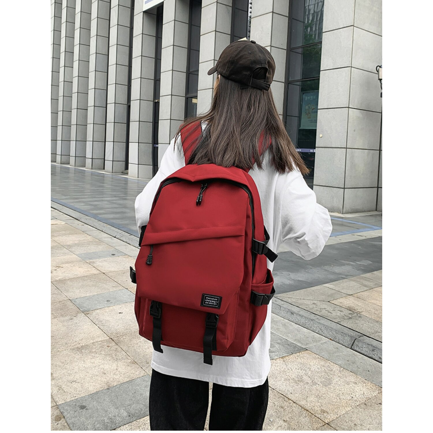 Eine Person mit rotem Rucksack steht vor einem Gebäude. Die Person trägt ein weißes Hemd.