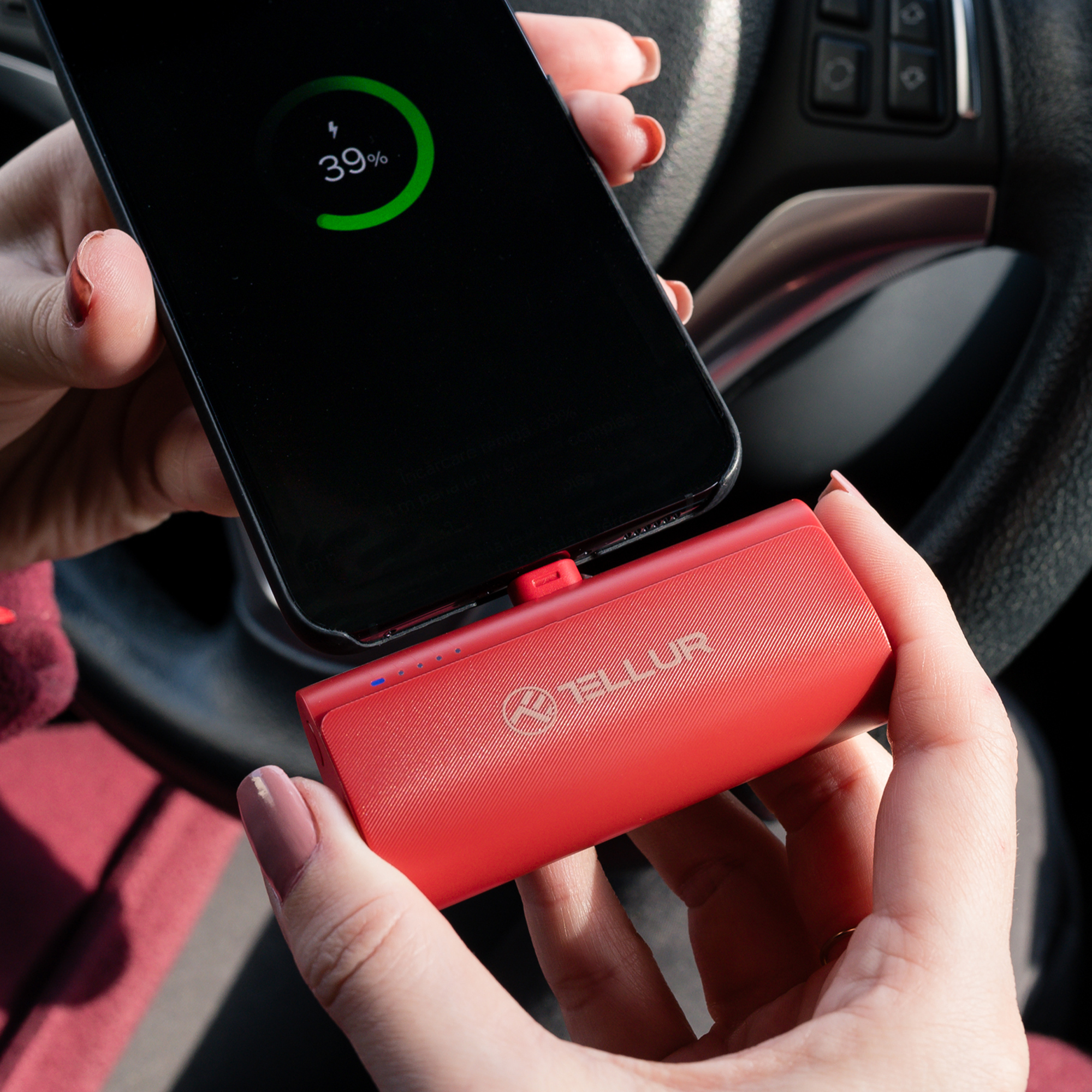 Dłonie trzymające telefon ładujący się z czerwonego power banku w samochodzie.