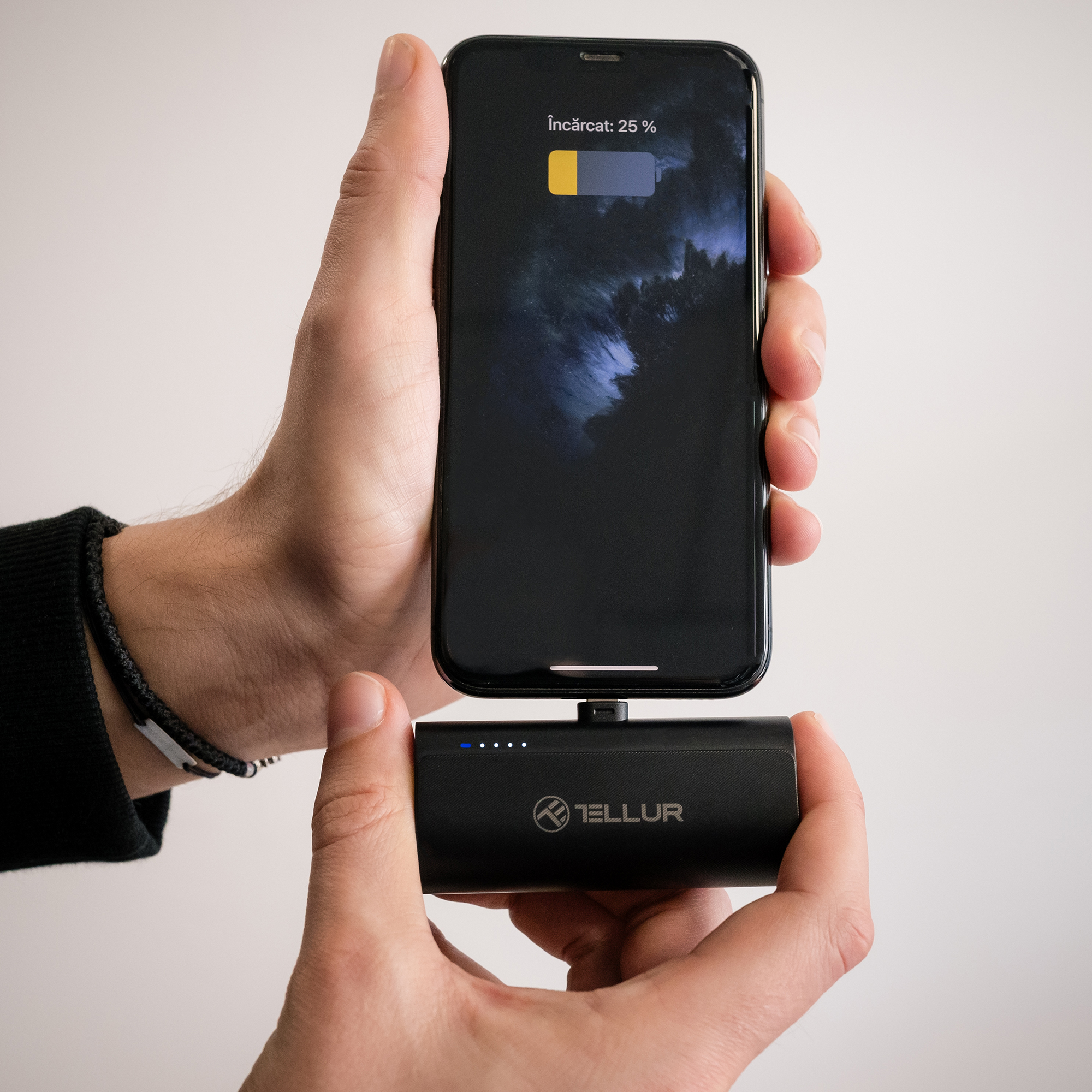 Ręce trzymają telefon podłączony do czarnego power banku, pokazując 25% naładowania.