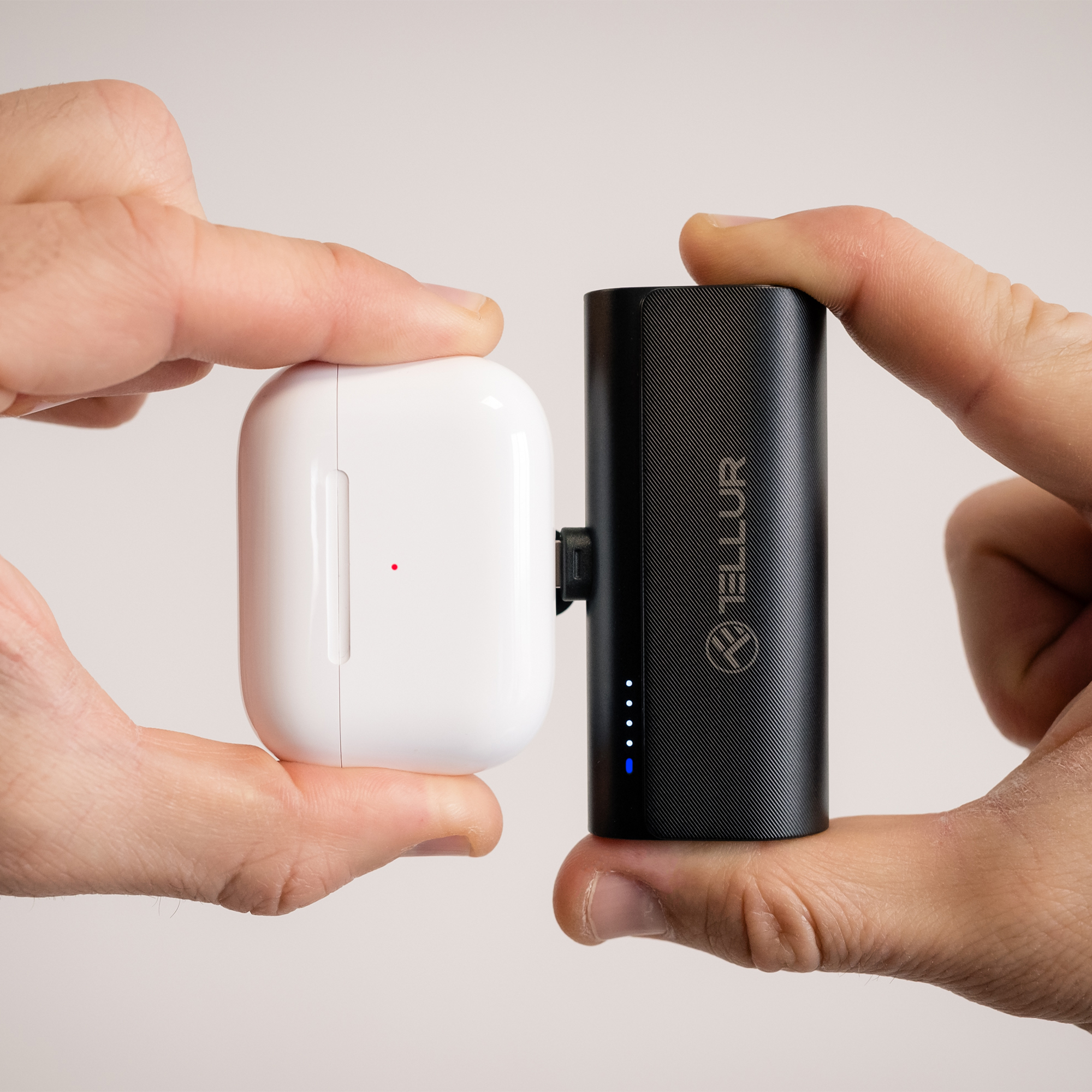 Dłonie trzymające białe etui na słuchawki i czarne, cylindryczne urządzenie ładujące.