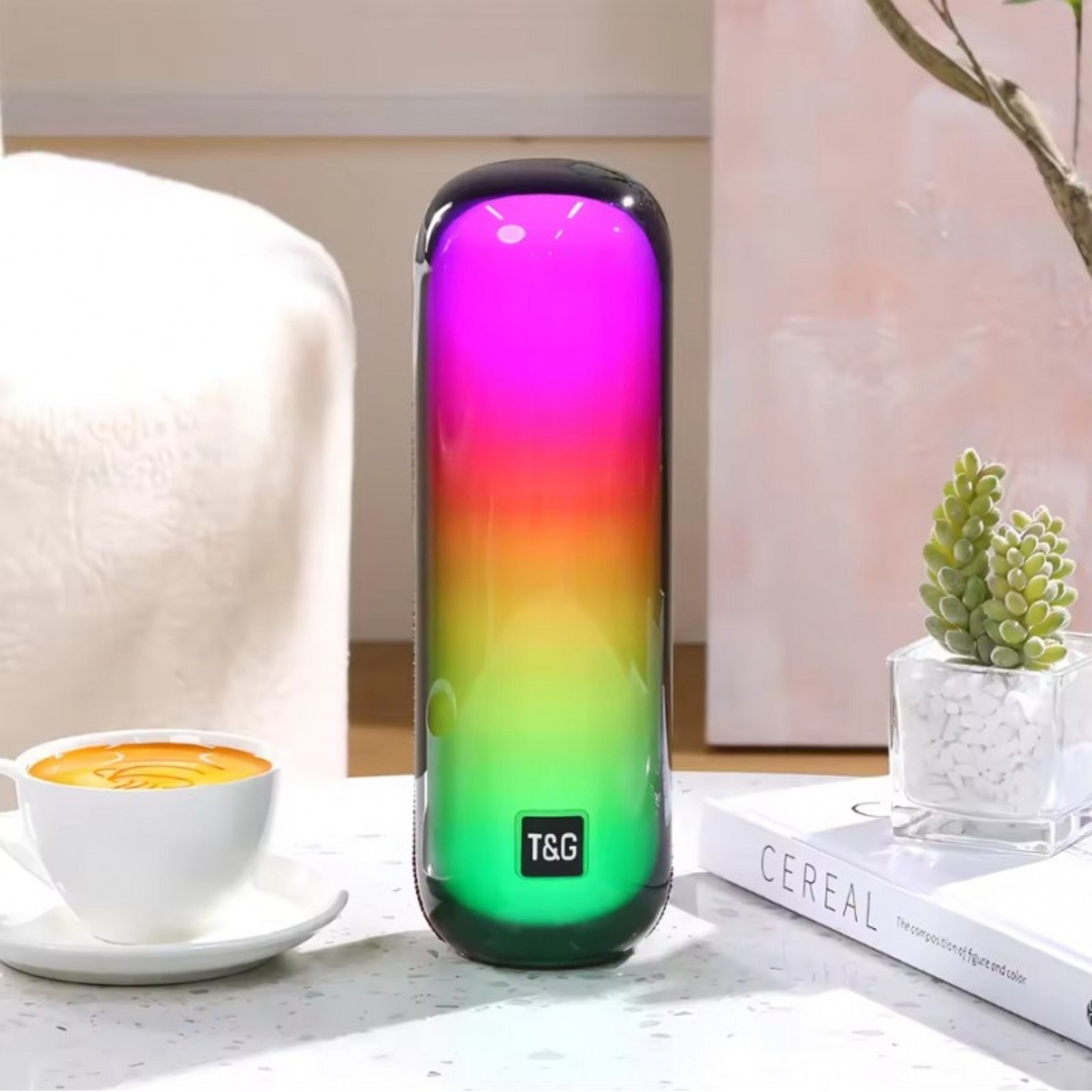 Un altavoz colorido con un gradiente de colores, con una taza de café y una pequeña planta en una mesa.