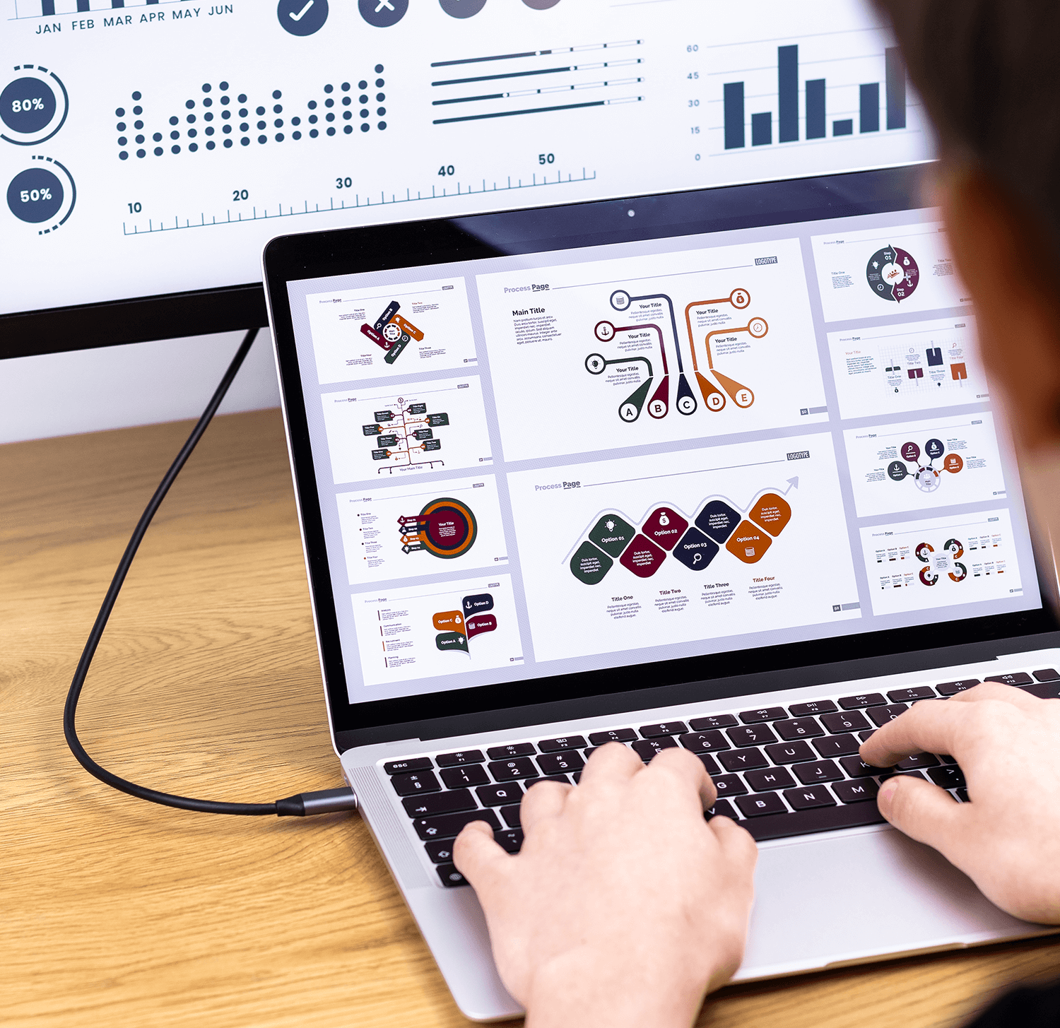 Osoba korzystająca z laptopa z prezentacją na ekranie, podłączonego do innego monitora. Drewniany stół.