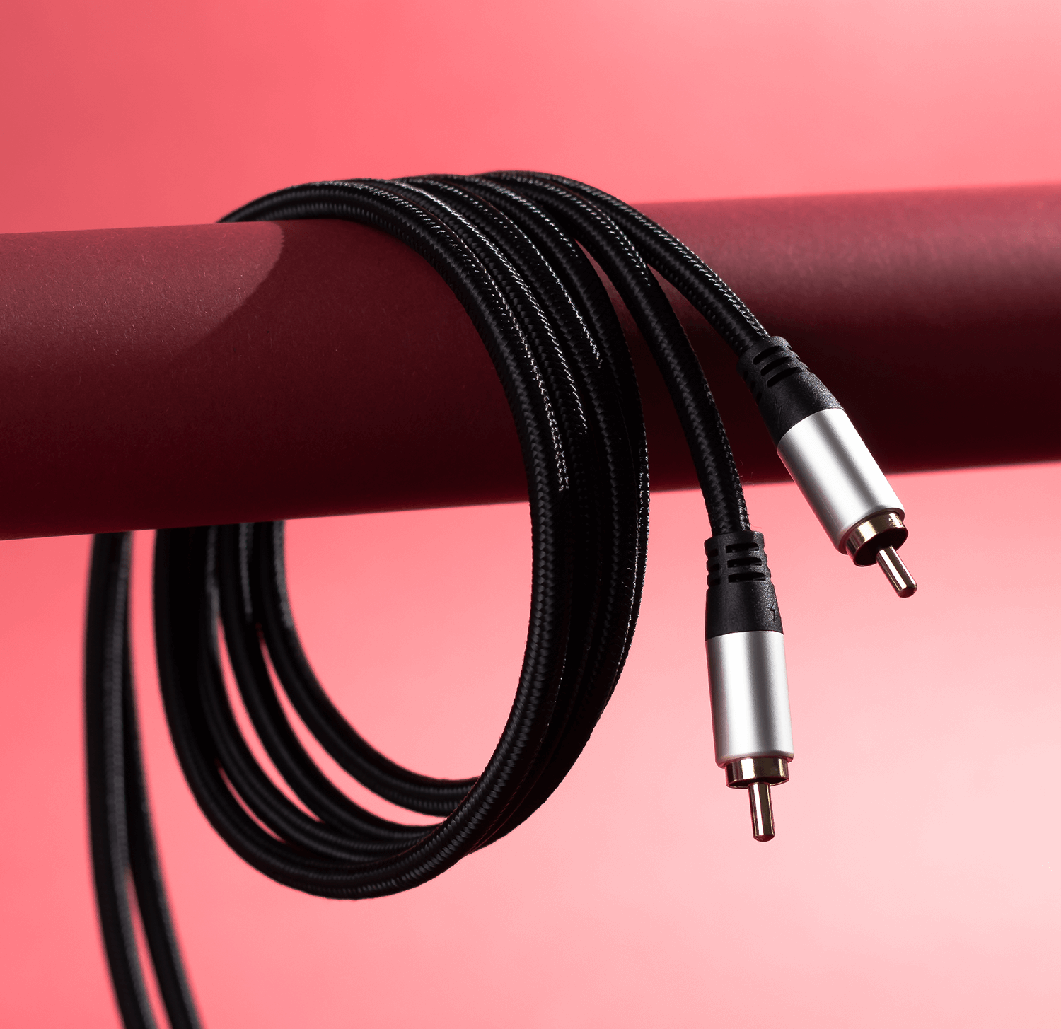 Cavi audio neri, arrotolati, con connettori argentati su sfondo rosso.