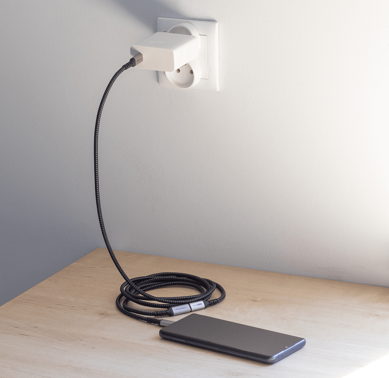 Konfiguracja ładowania telefonu: kabel, ładowarka i telefon na drewnianej powierzchni.