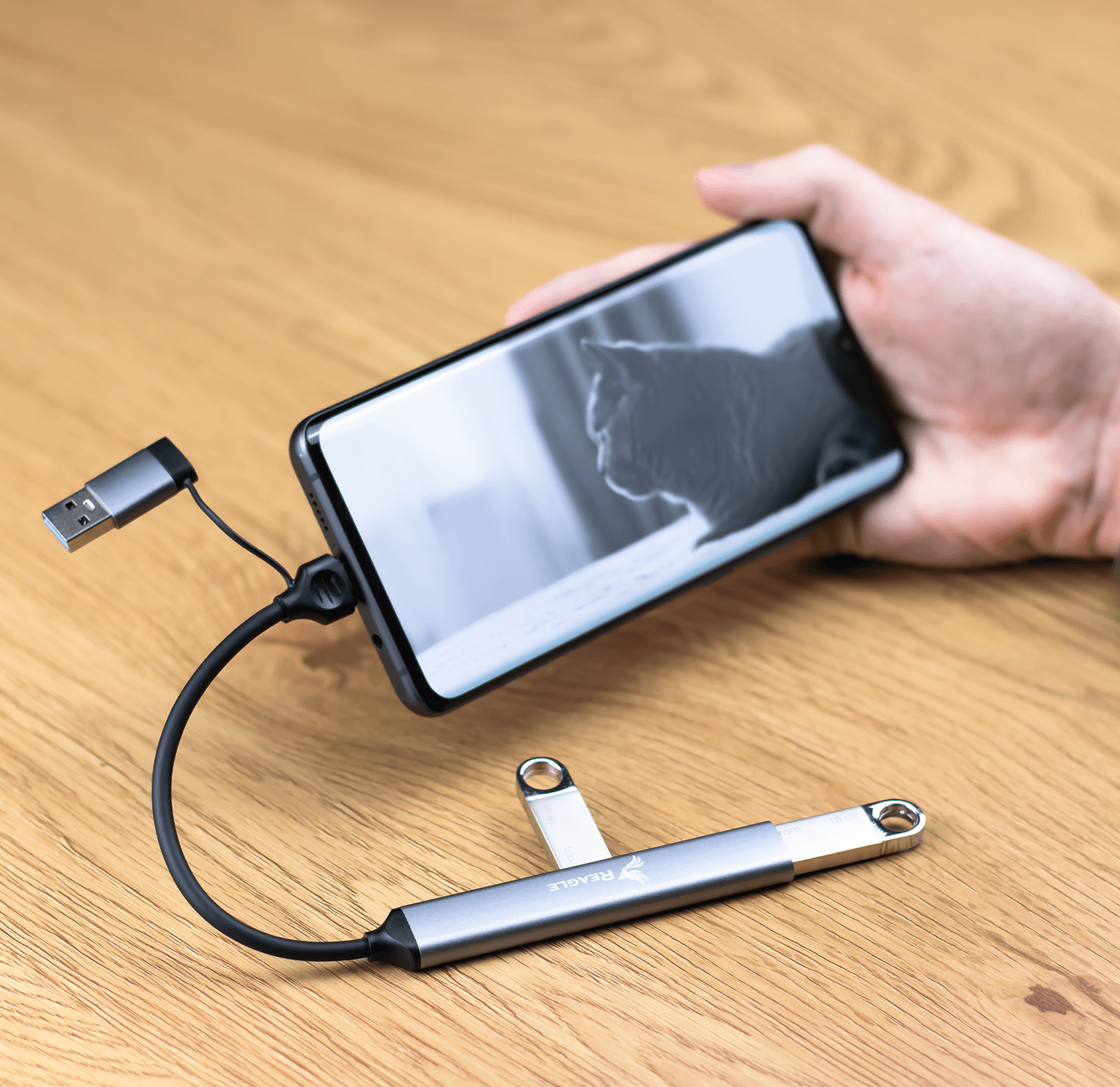 Kabel USB-C podłączony do telefonu i dysku USB na drewnianej powierzchni.