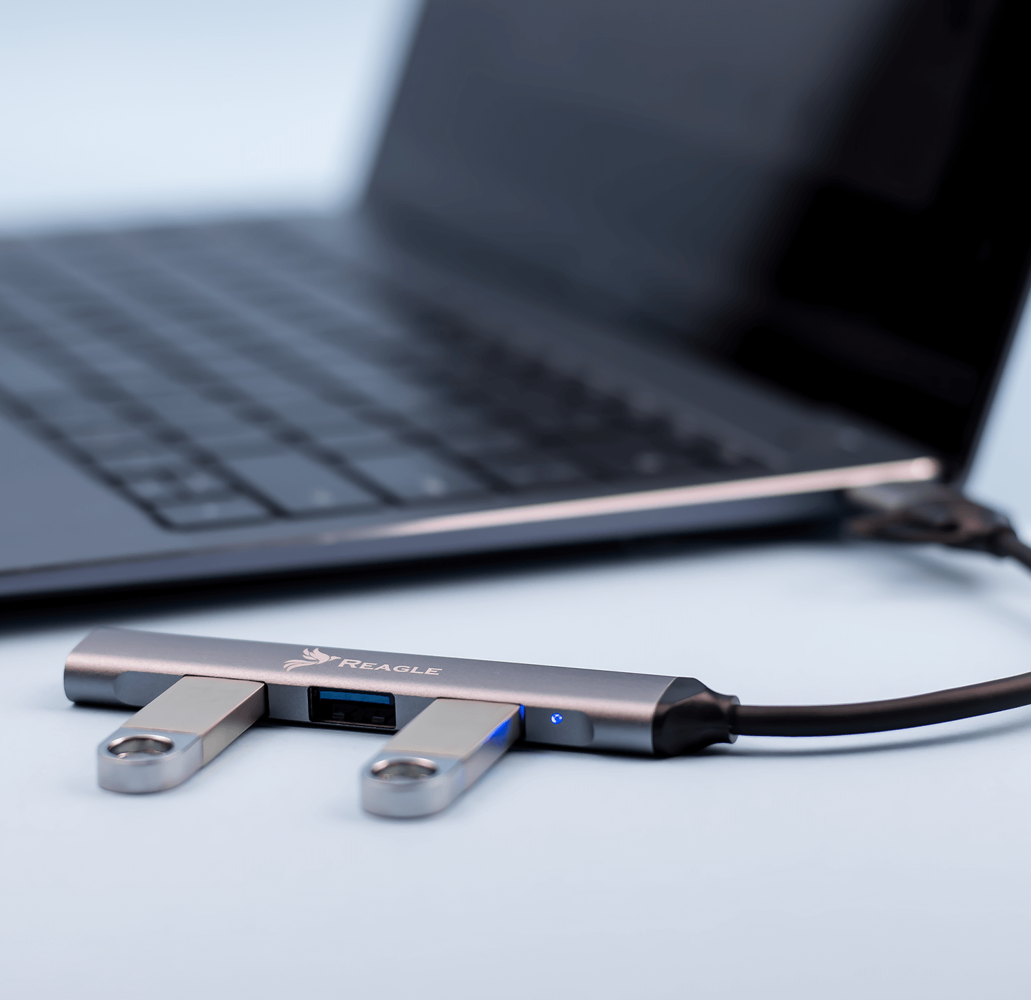 Srebrny hub USB z dwoma złączami USB i laptopem w tle.