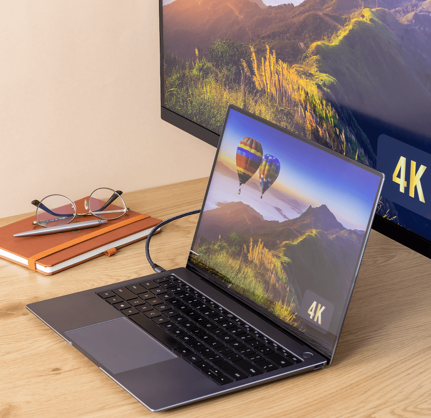 Laptop na drewnianym biurku, wyświetlający krajobraz. Okulary, notatnik i monitor z obrazem 4K.