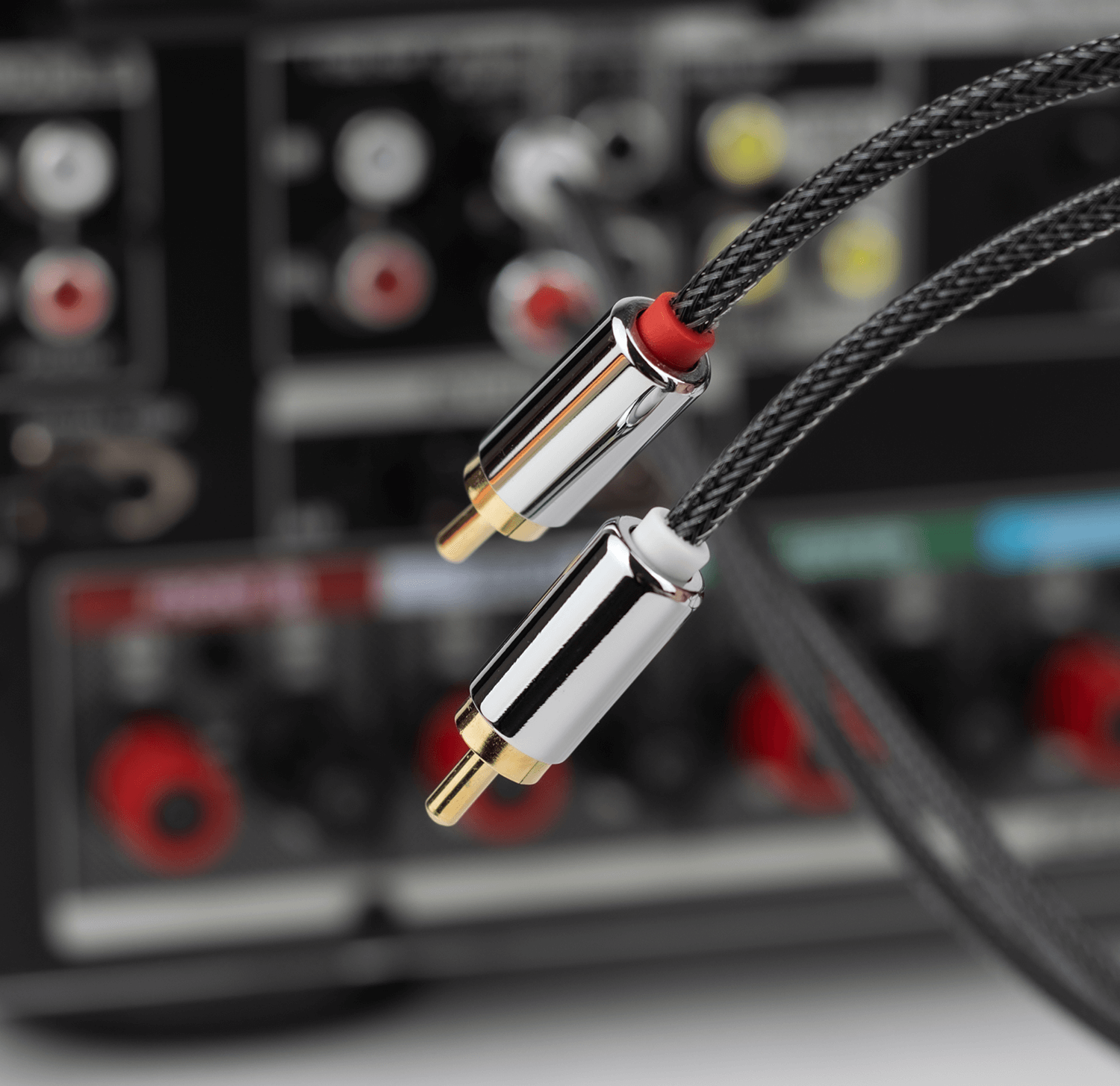 Dwa kable audio ze srebrnymi i złotymi złączami są podłączone do tyłu czarnego odbiornika stereo.