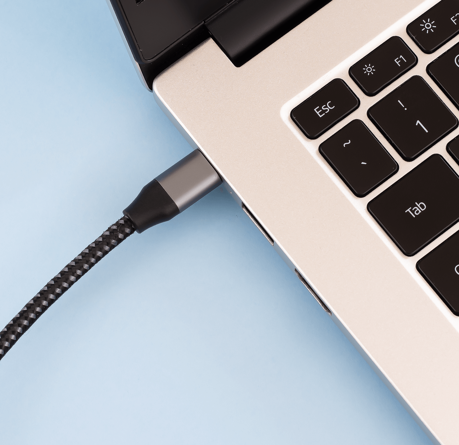 Laptop z podłączonym kablem USB-C, srebrny laptop, niebieskie tło.