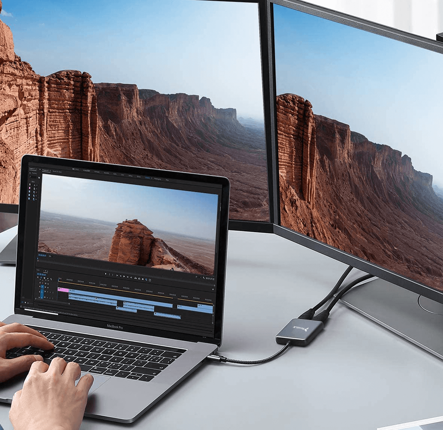 Osoba pracująca na laptopie podłączonym do dwóch zewnętrznych monitorów, pokazująca krajobraz kanionu.