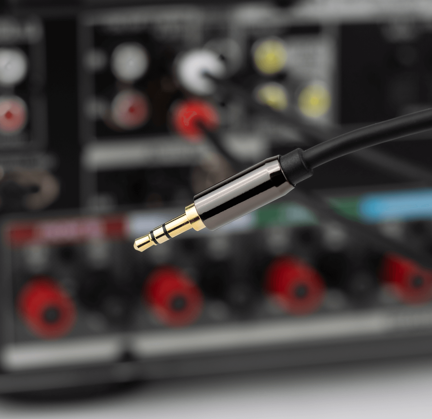 Zbliżenie wtyczki audio 3,5 mm ze złotą końcówką, podłączonej do czarnego urządzenia.