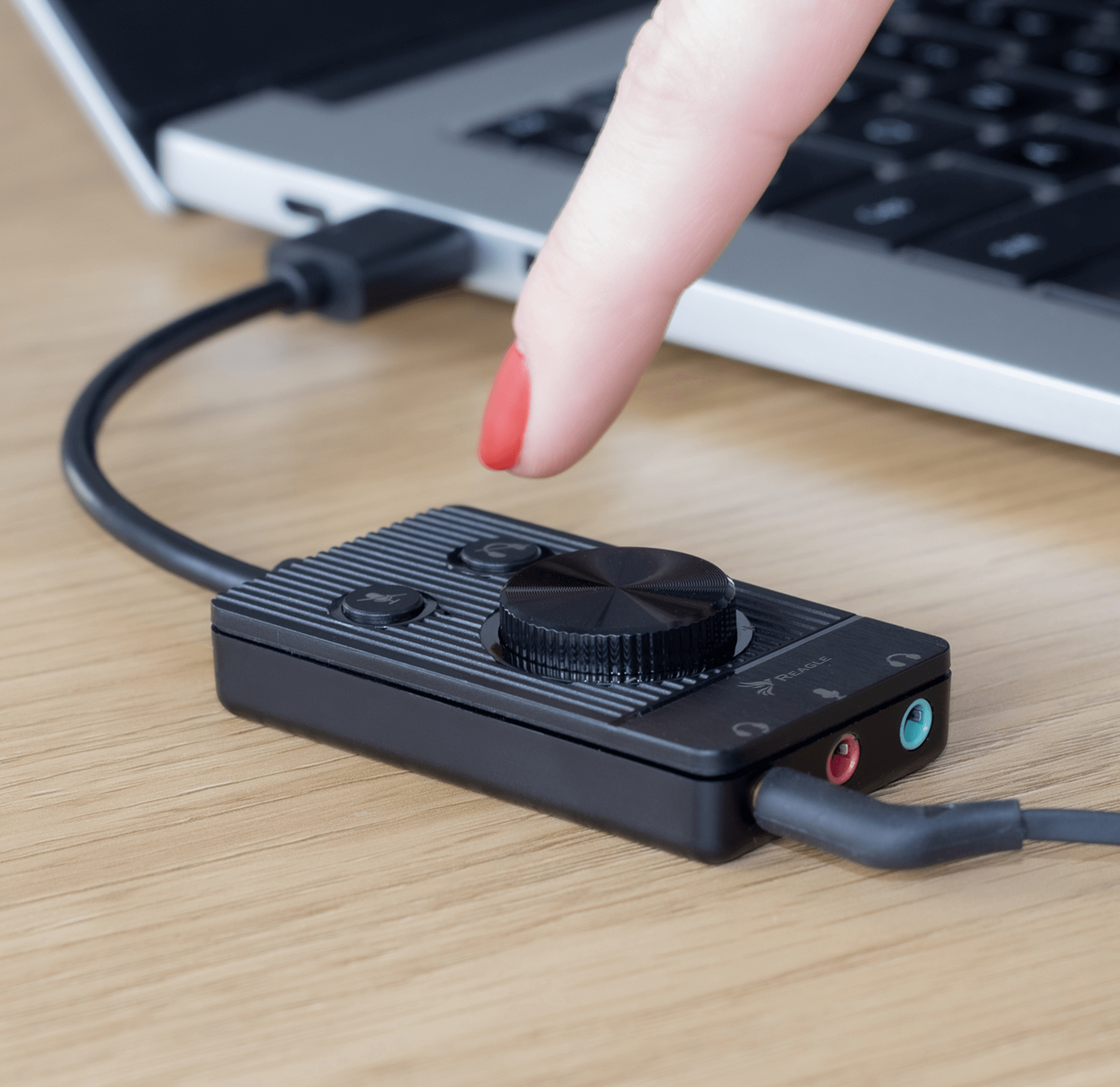 Palec dotyka czarnego urządzenia audio. Laptop w tle. Kabel USB.