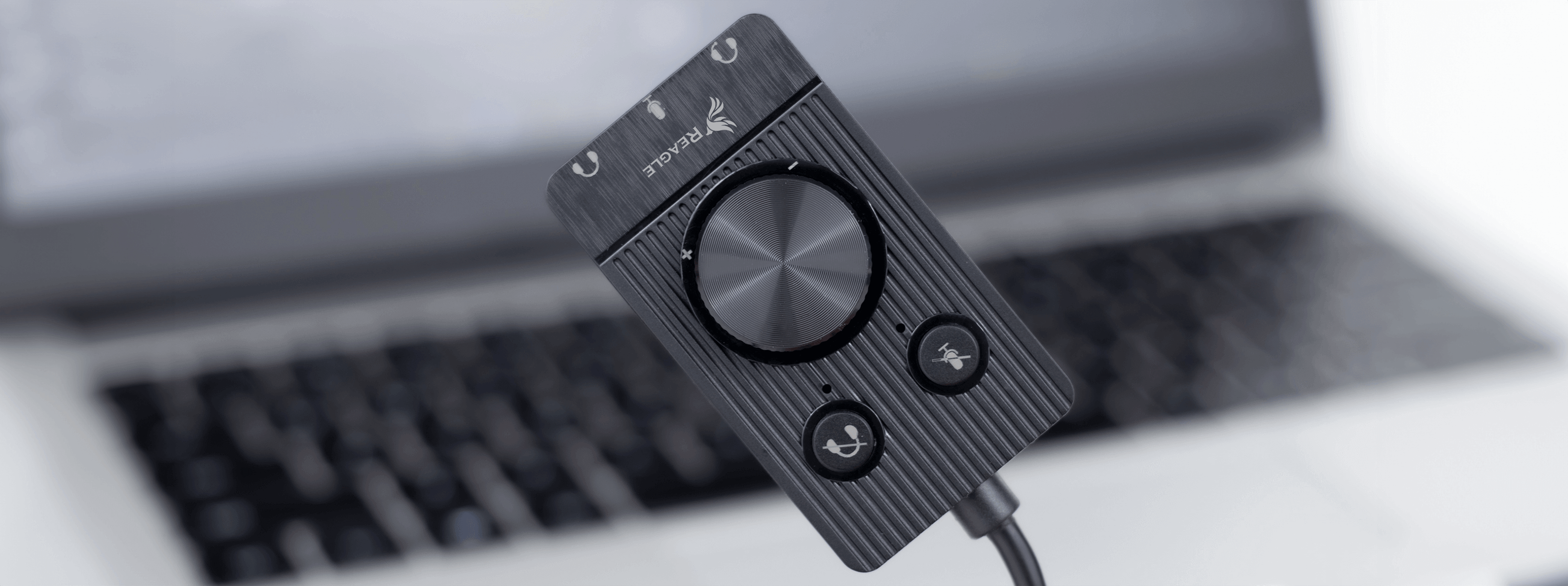 Czarny interfejs audio, panel sterowania z pokrętłami, przyciskami i połączeniami, na klawiaturze laptopa.