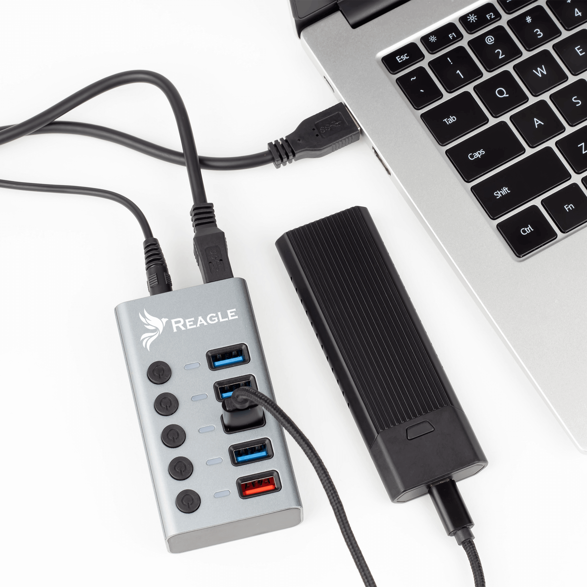 Srebrny hub z portami USB i czarną ładowarką podłączoną do laptopa. Wszystko na białym tle.