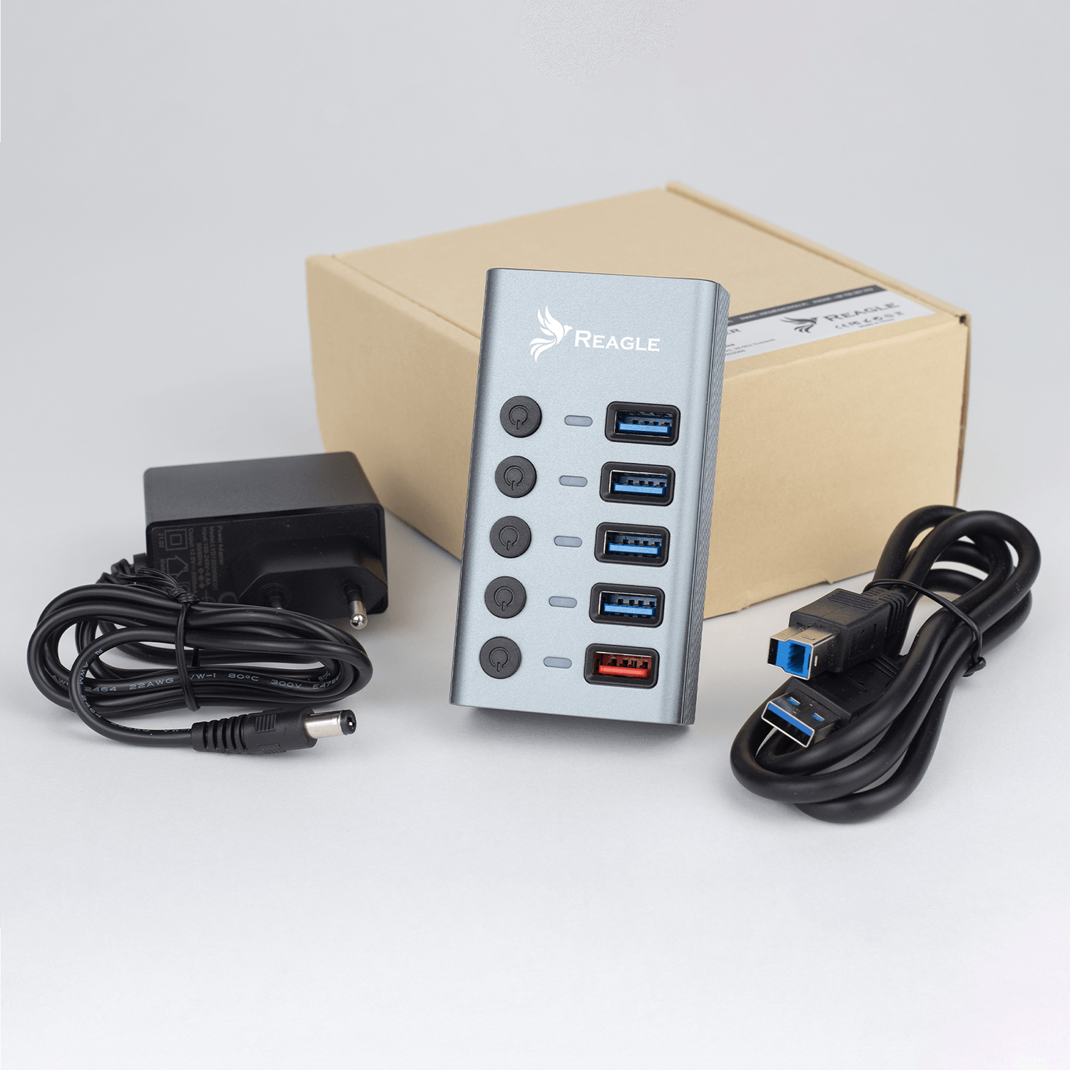 Hub USB REAGLE z zasilaczem, kablem i pudełkiem. Szary hub z portami, czarny zasilacz, kabel USB.