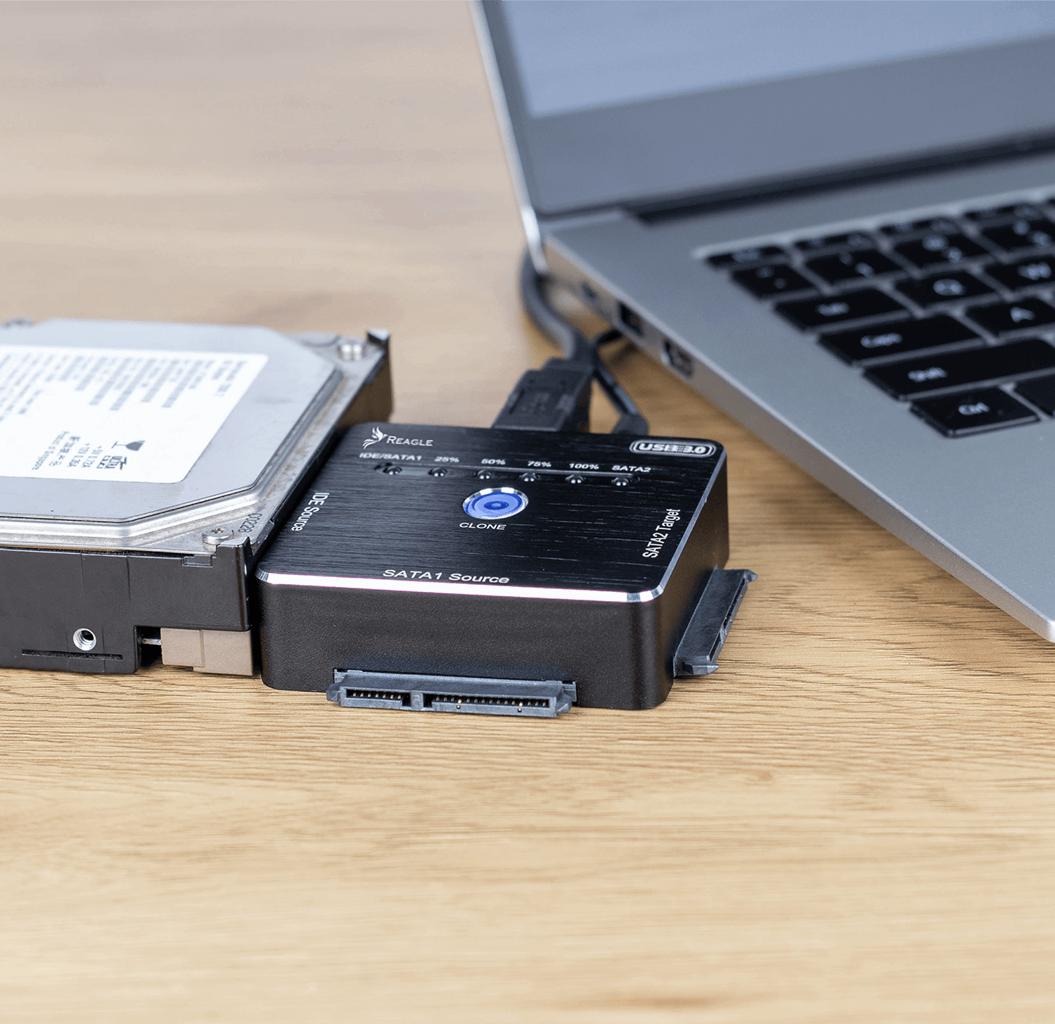 Dysk twardy podłączony do urządzenia. Laptop jest w tle na drewnianym stole.