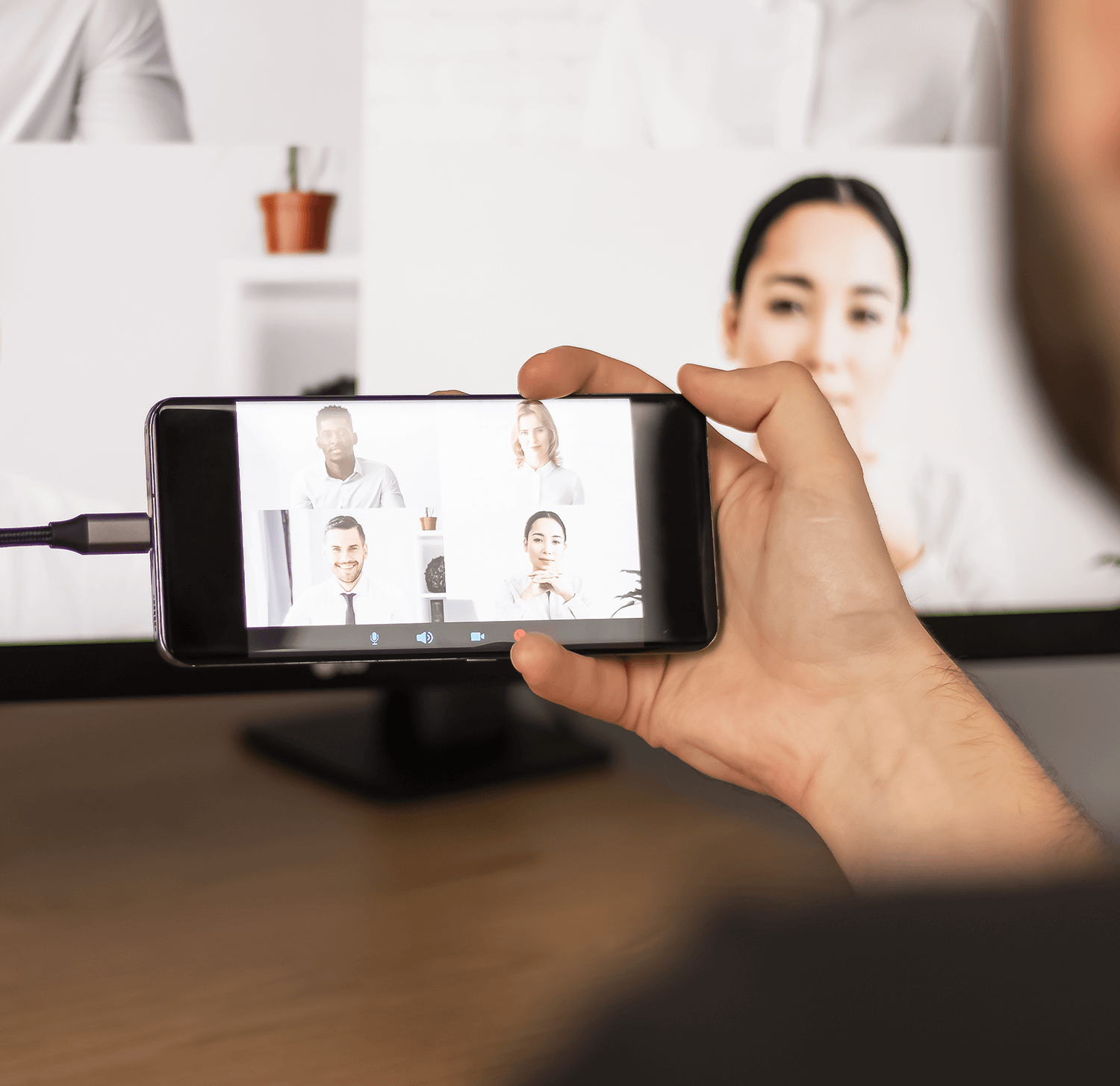 Dłoń trzymająca telefon, na którym wyświetlana jest rozmowa wideo z 5 uczestnikami na ekranie.