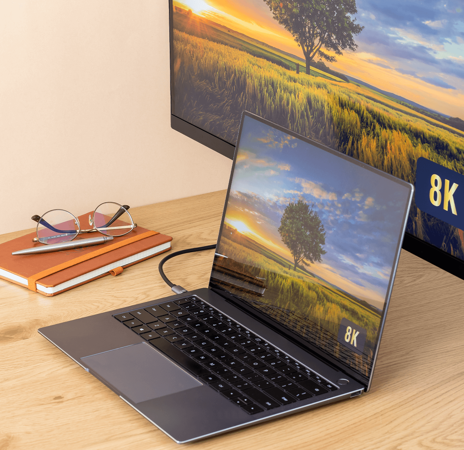 Laptop na biurku podłączony do monitora. Okulary i notatnik również na biurku.