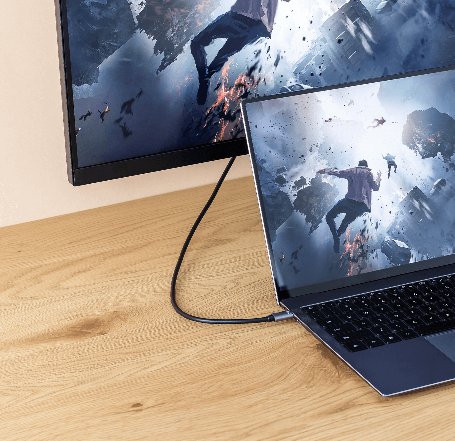 Laptop podłączony do monitora, drewniany stół, scena akcji na ekranach.