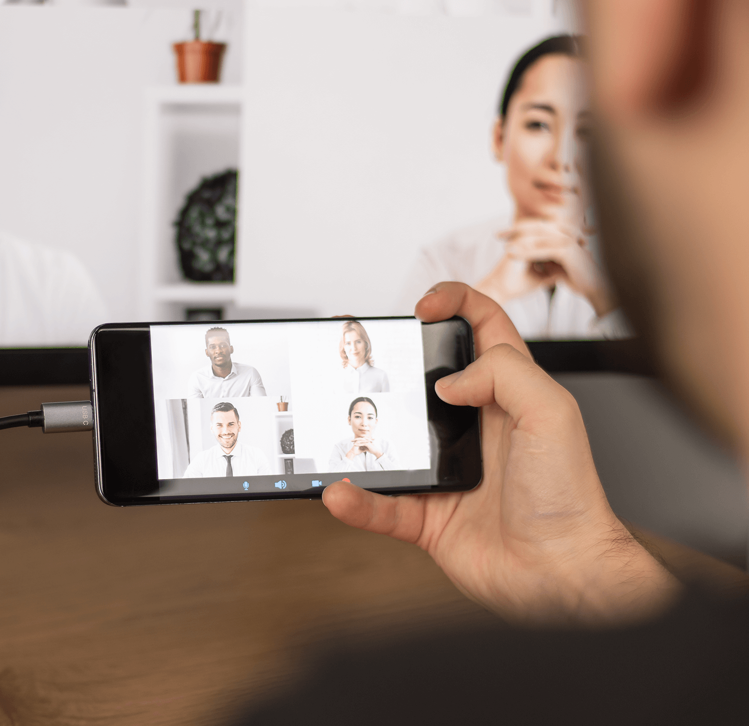 Osoba trzymająca telefon z rozmową wideo z wieloma uczestnikami na ekranie.