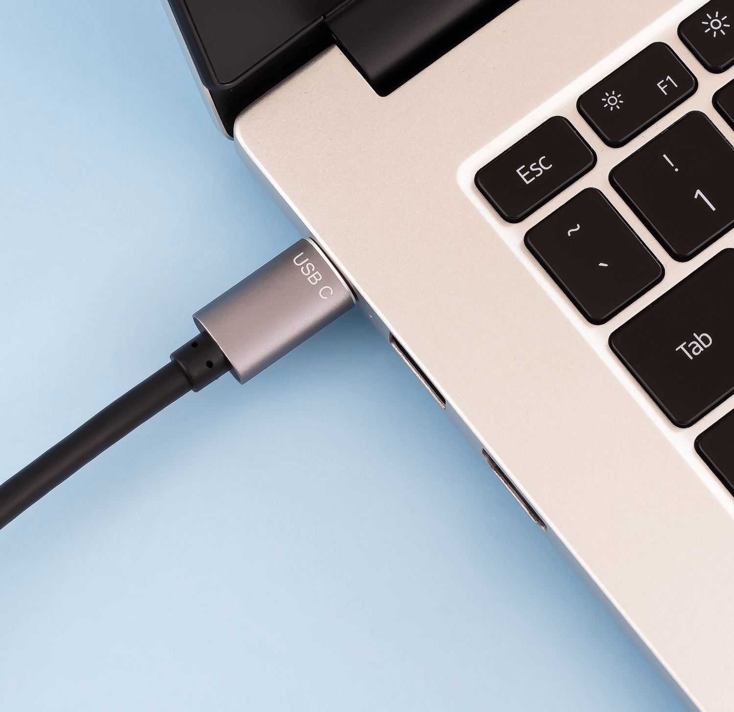 Kabel USB-C jest podłączony do laptopa. Widoczna jest klawiatura laptopa.