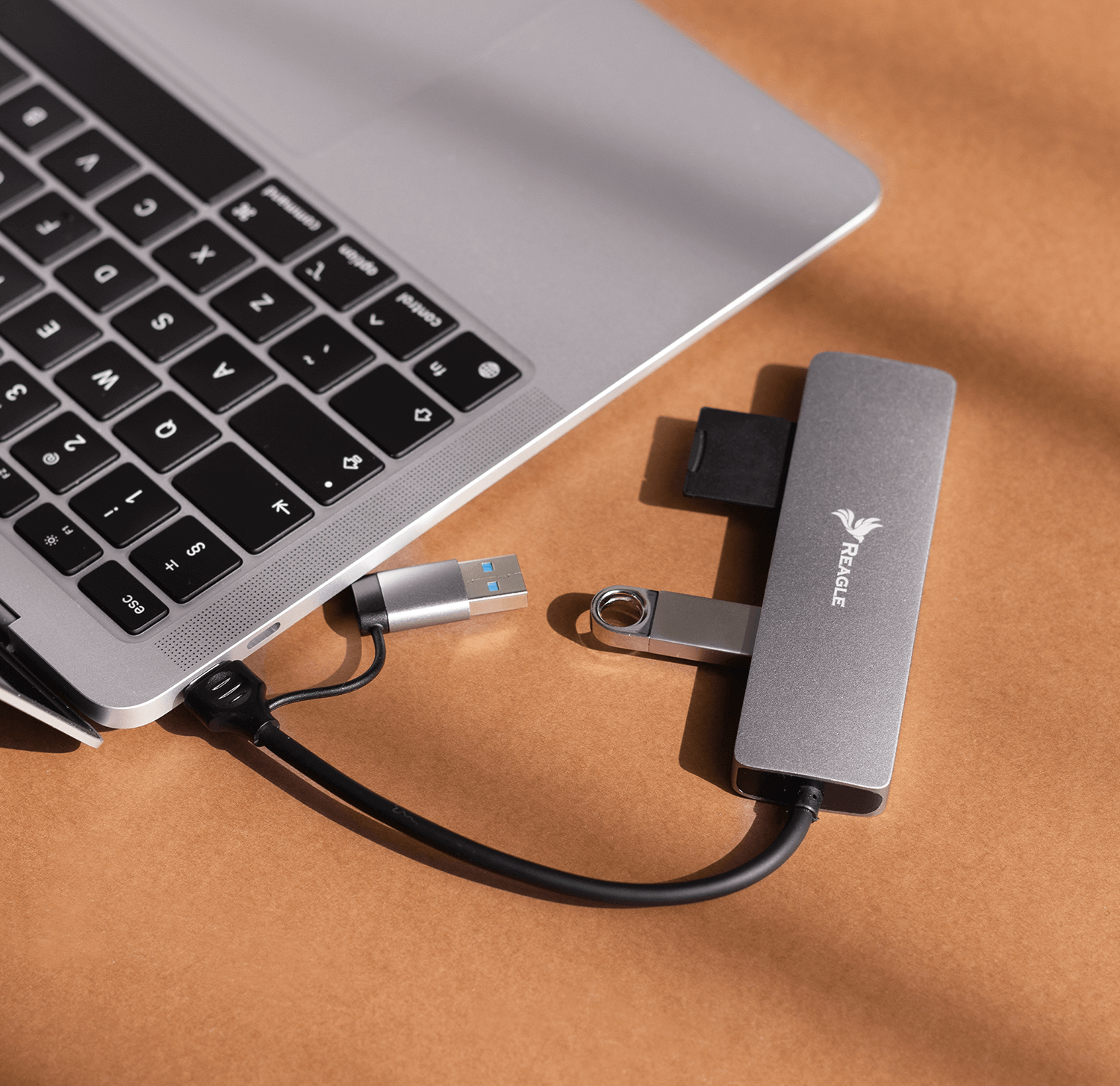 Laptop, hub USB i dysk USB na brązowej powierzchni.