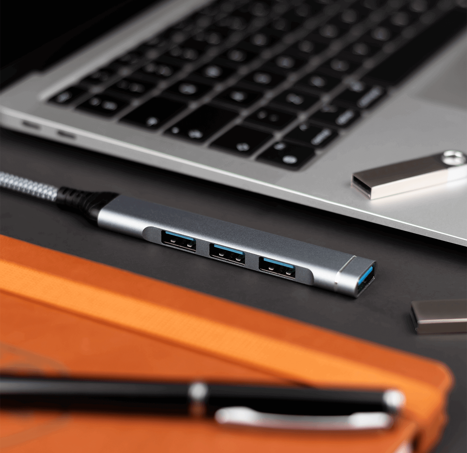 Hub USB z trzema portami, laptop i dwa dyski USB na ciemnej powierzchni.