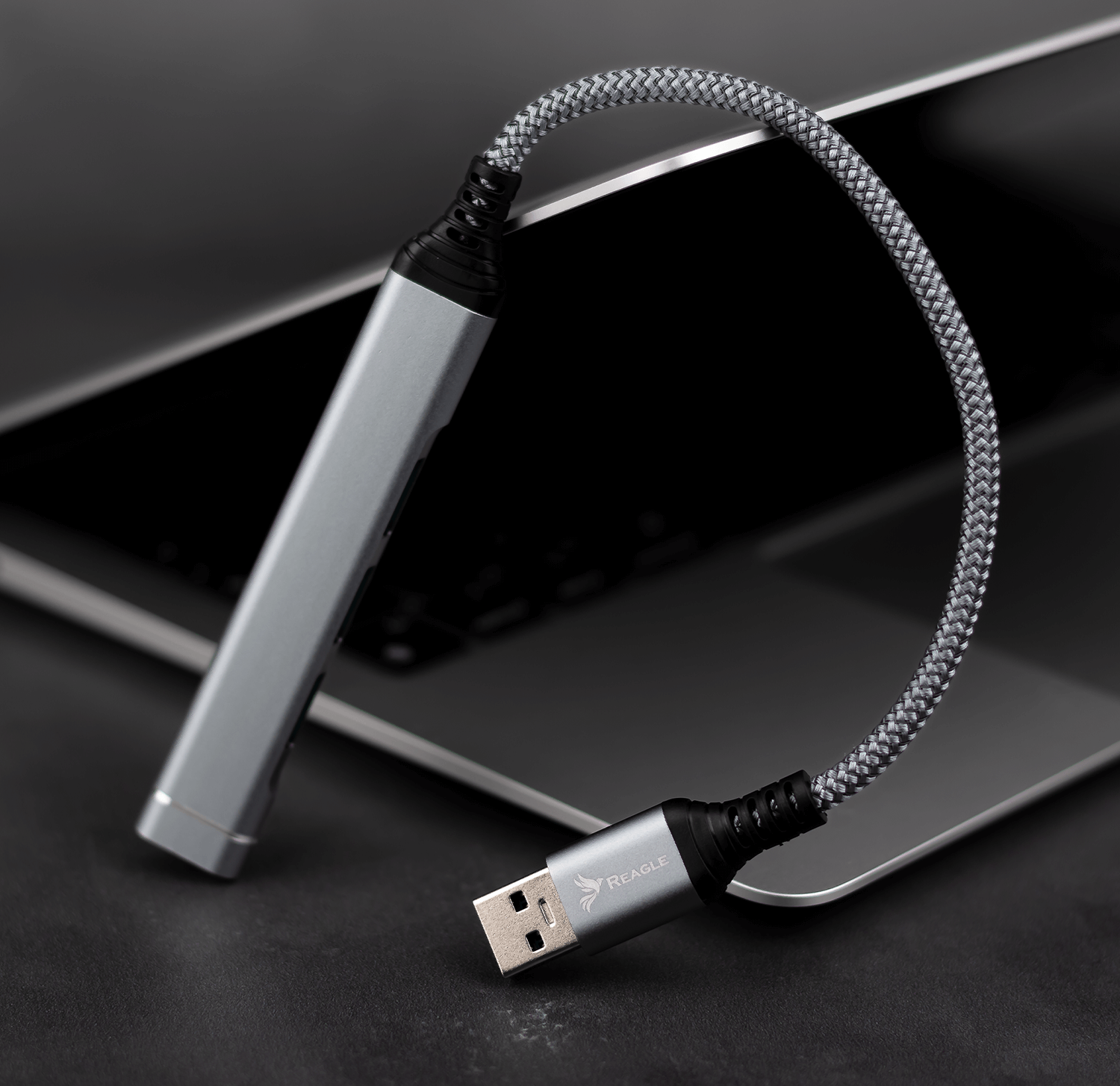 Szary kabel USB z czarnym złączem i portem USB. Leży na laptopie.