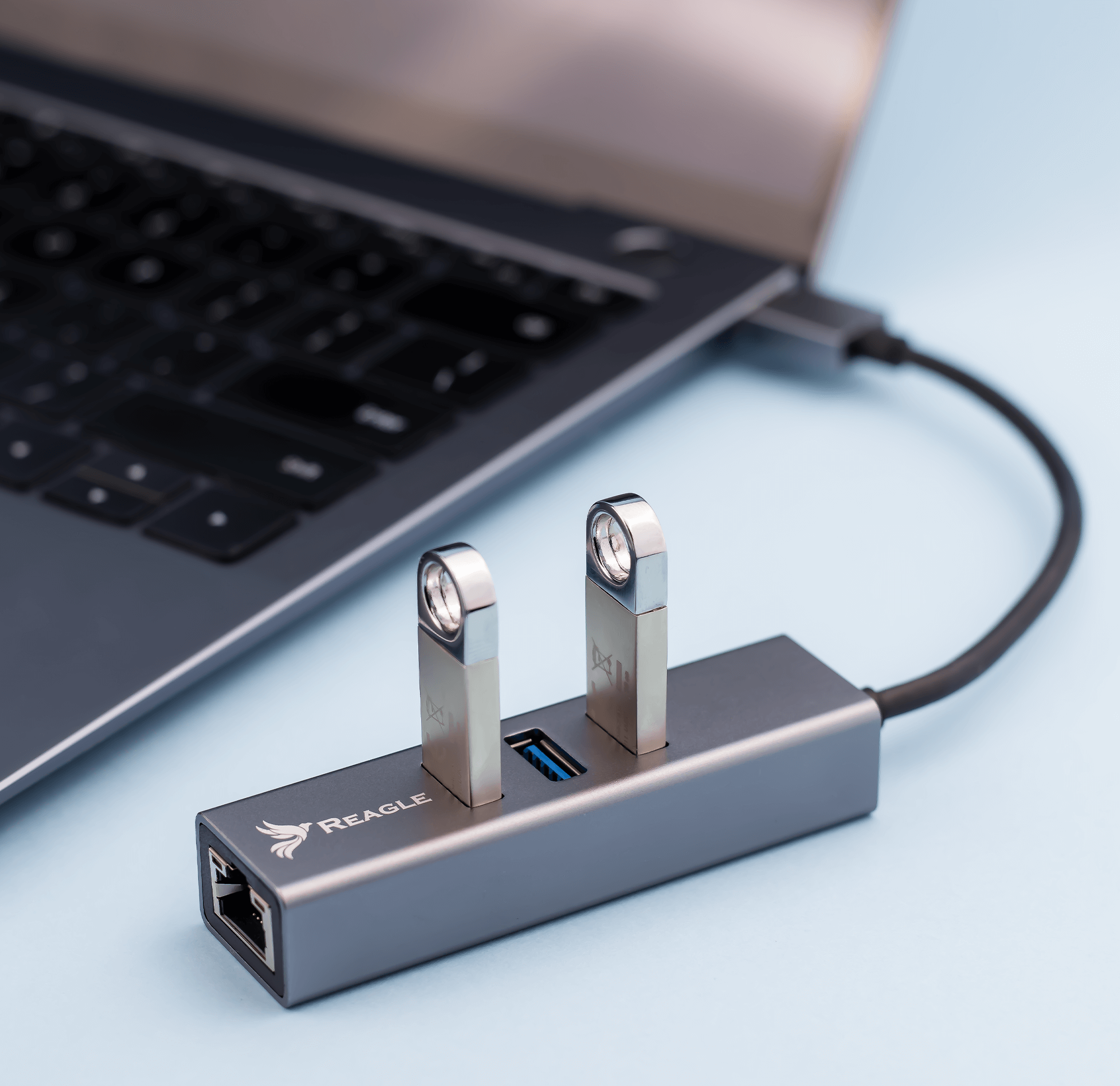 Szary hub USB z dwiema srebrnymi dyskami USB wpiętymi do niego. Laptop jest w tle.