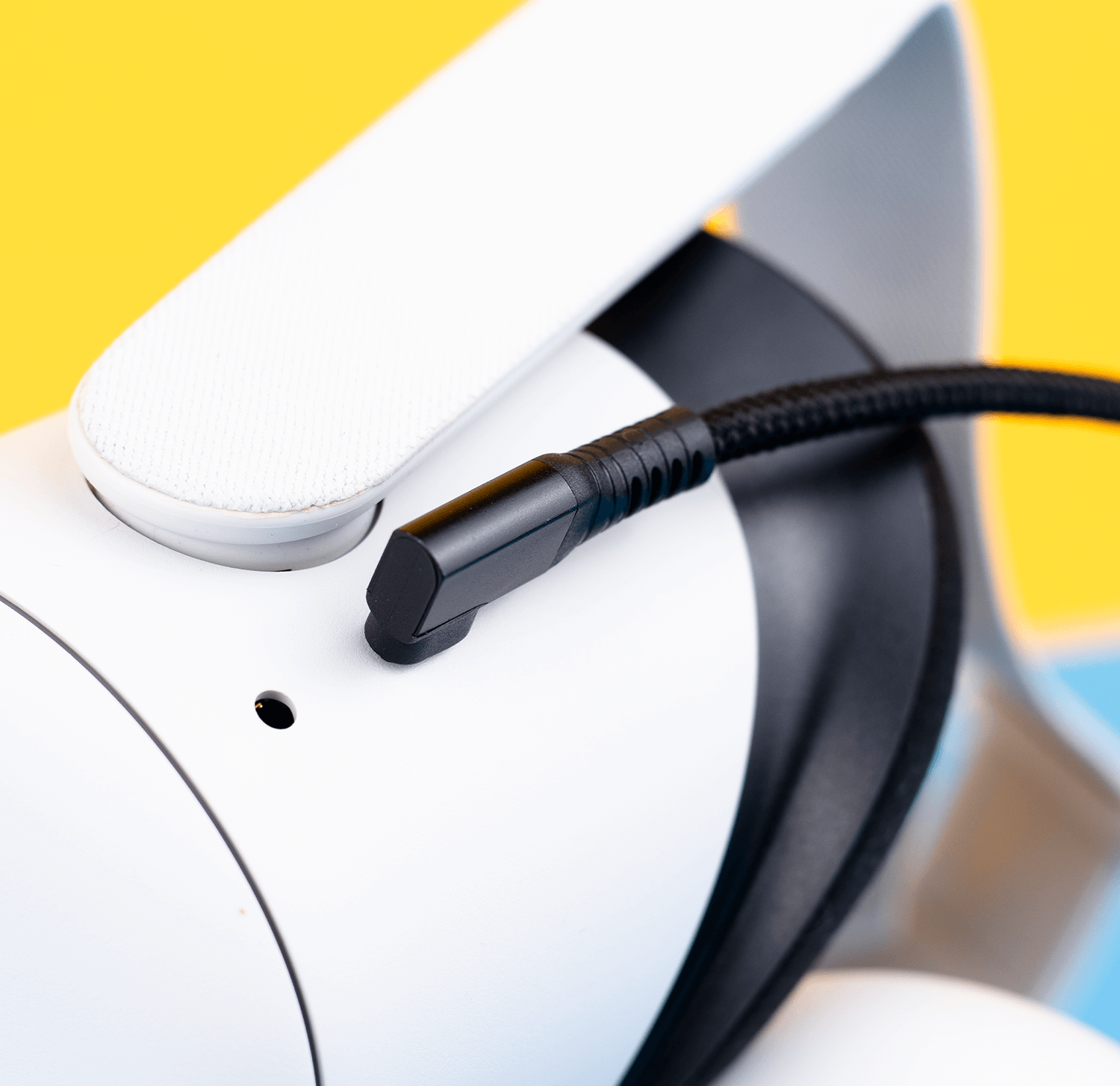 Zbliżenie białego zestawu słuchawkowego VR z czarnym kablem, na żółto-niebieskim tle.