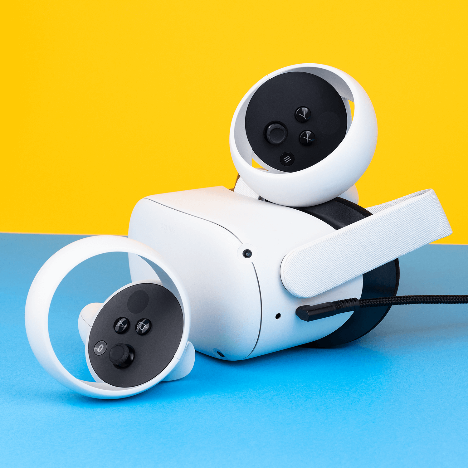 Biały zestaw VR z kontrolerami na niebieskim i żółtym tle. Czarne przyciski i kabel są widoczne.