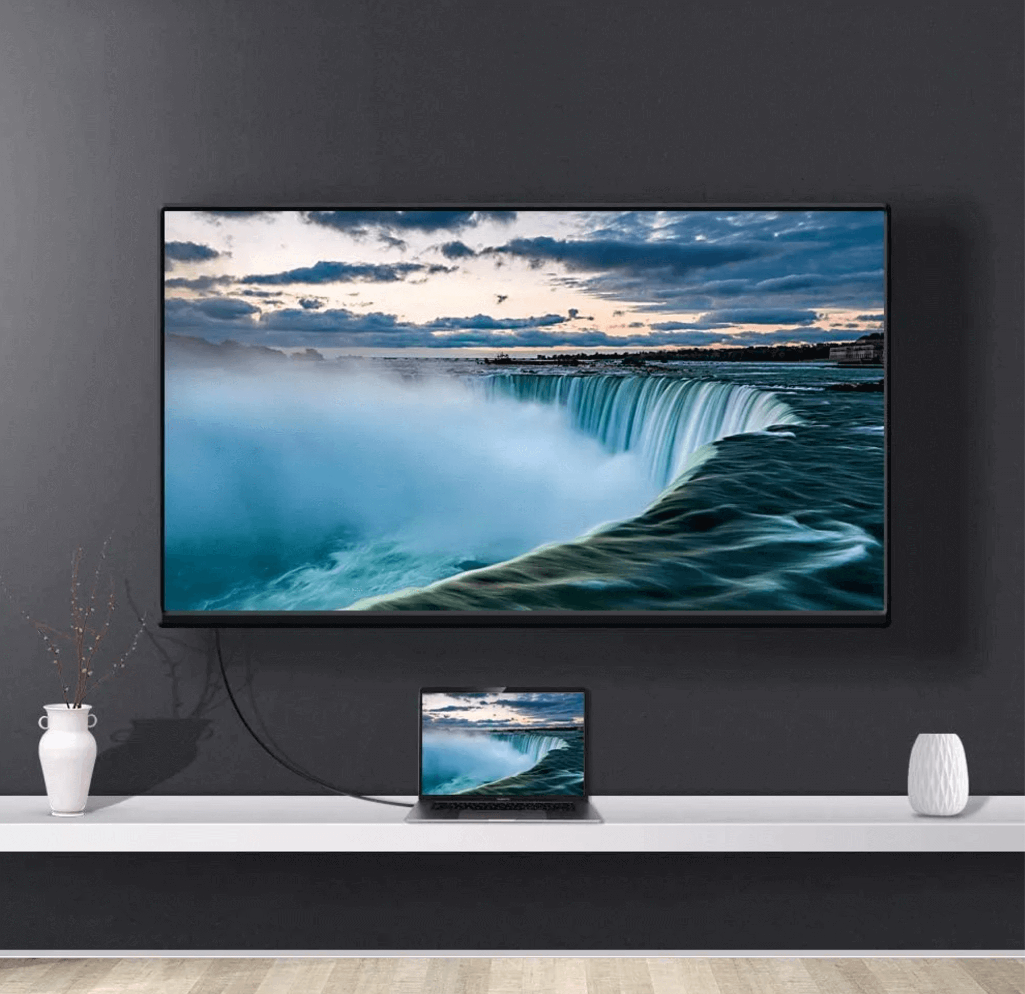 Telewizor pokazujący wodospad Niagara nad laptopem. Telewizor jest zamontowany na czarnej ścianie z białymi elementami dekoracyjnymi.