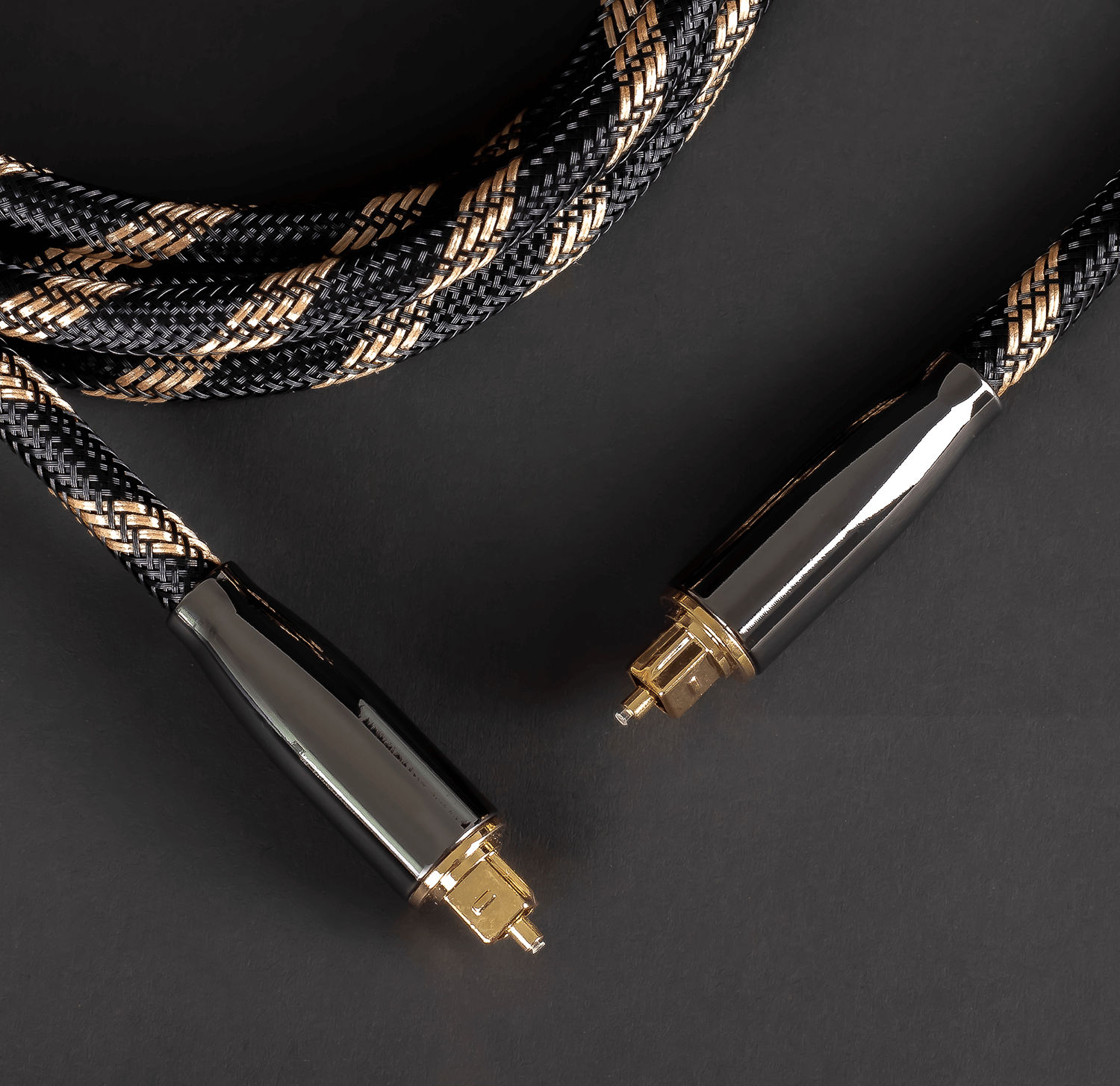 Dwa czarno-złote kable audio ze złączami na ciemnej powierzchni.
