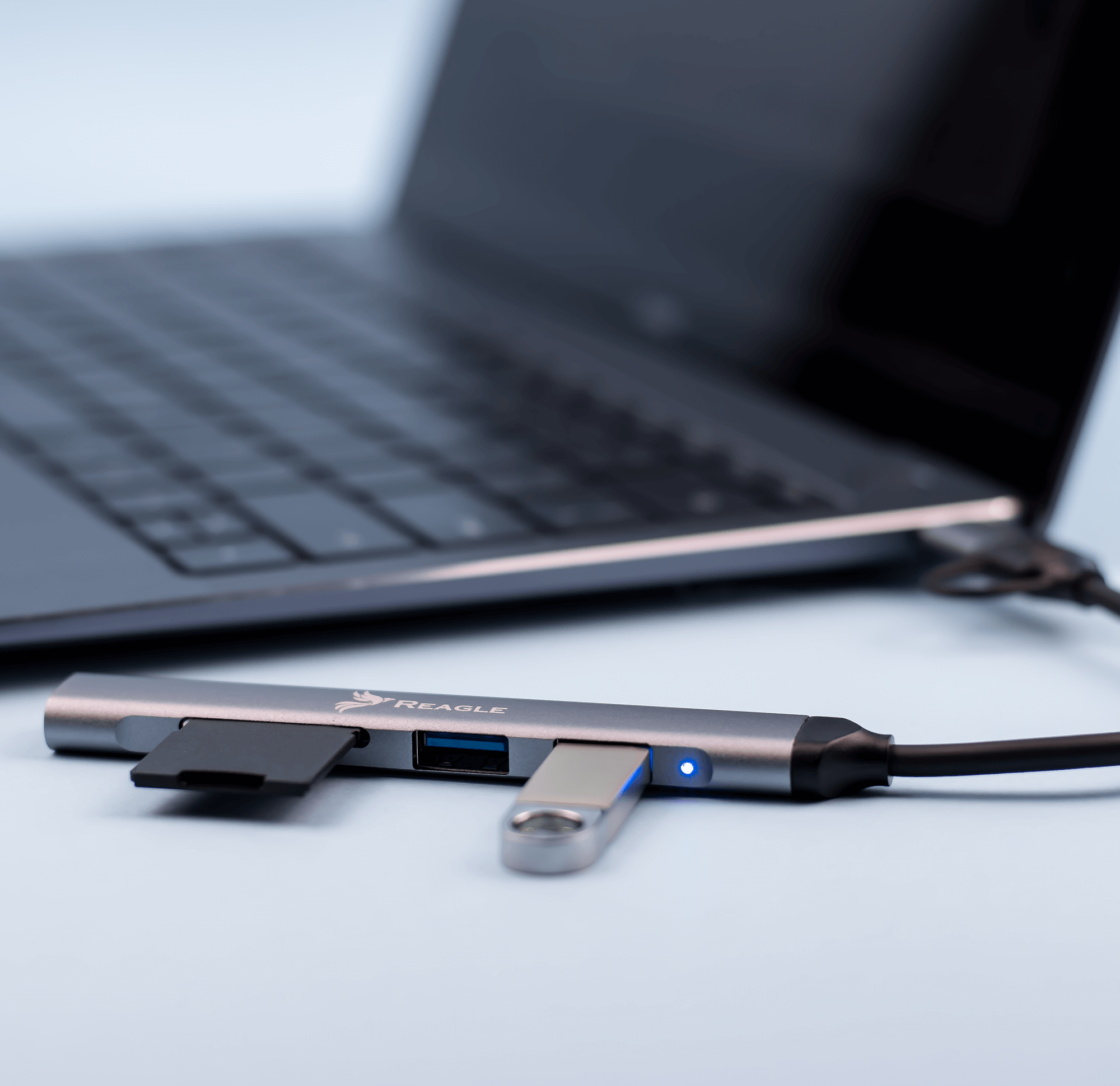 Un hub argentato con porta USB, scheda SD e USB-C collegato a un laptop. Una luce blu indica l'attività.