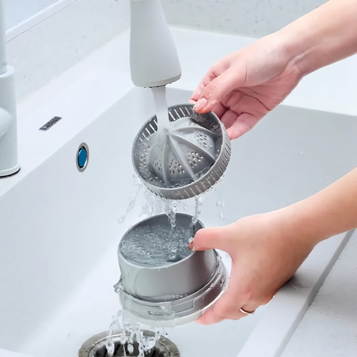 Manos lavando un exprimidor de cítricos gris en un fregadero blanco. El agua corre hacia el fregadero.