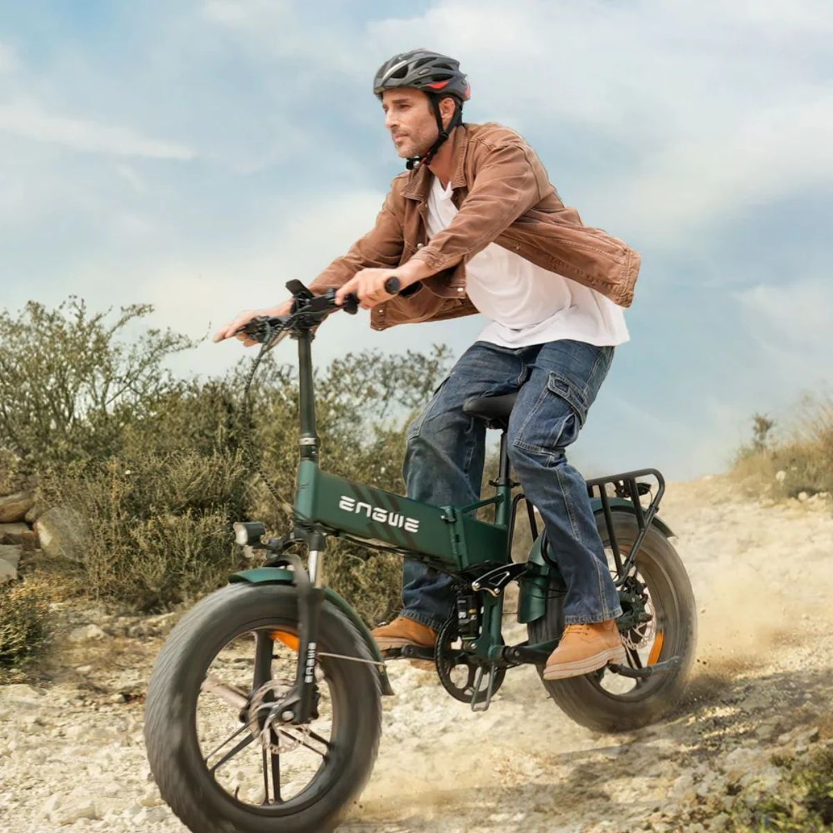 Ein Mann fährt mit einem grünen Elektrofahrrad auf einer unbefestigten Straße. Er trägt eine braune Jacke und Jeans.