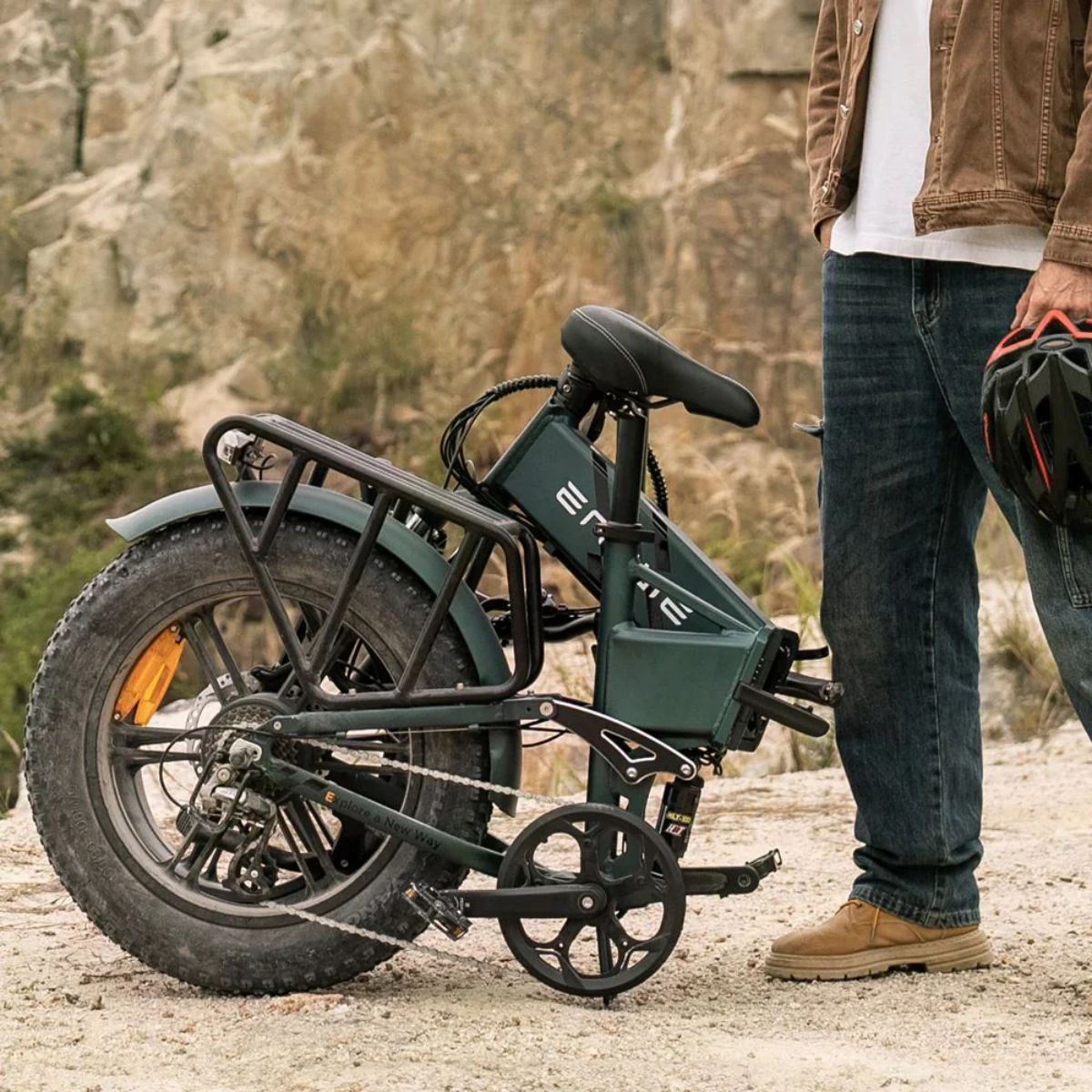 Grünes, zusammenklappbares Elektrofahrrad, mit einer Person, die einen Helm hält. Hintergrund ist felsig.
