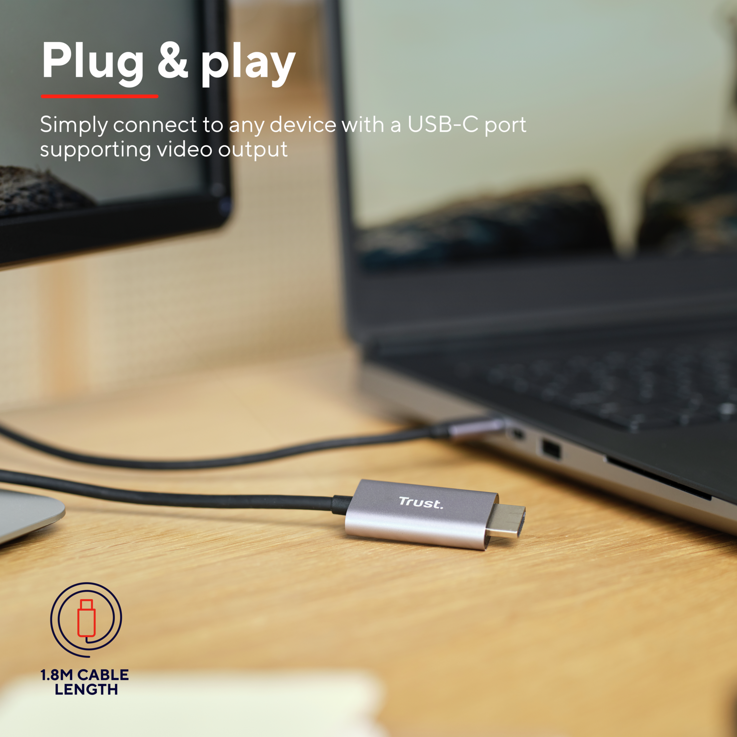 Cable USB-C a USB-C conectado a un portátil, adaptador plateado 'Trust', superficie de madera.