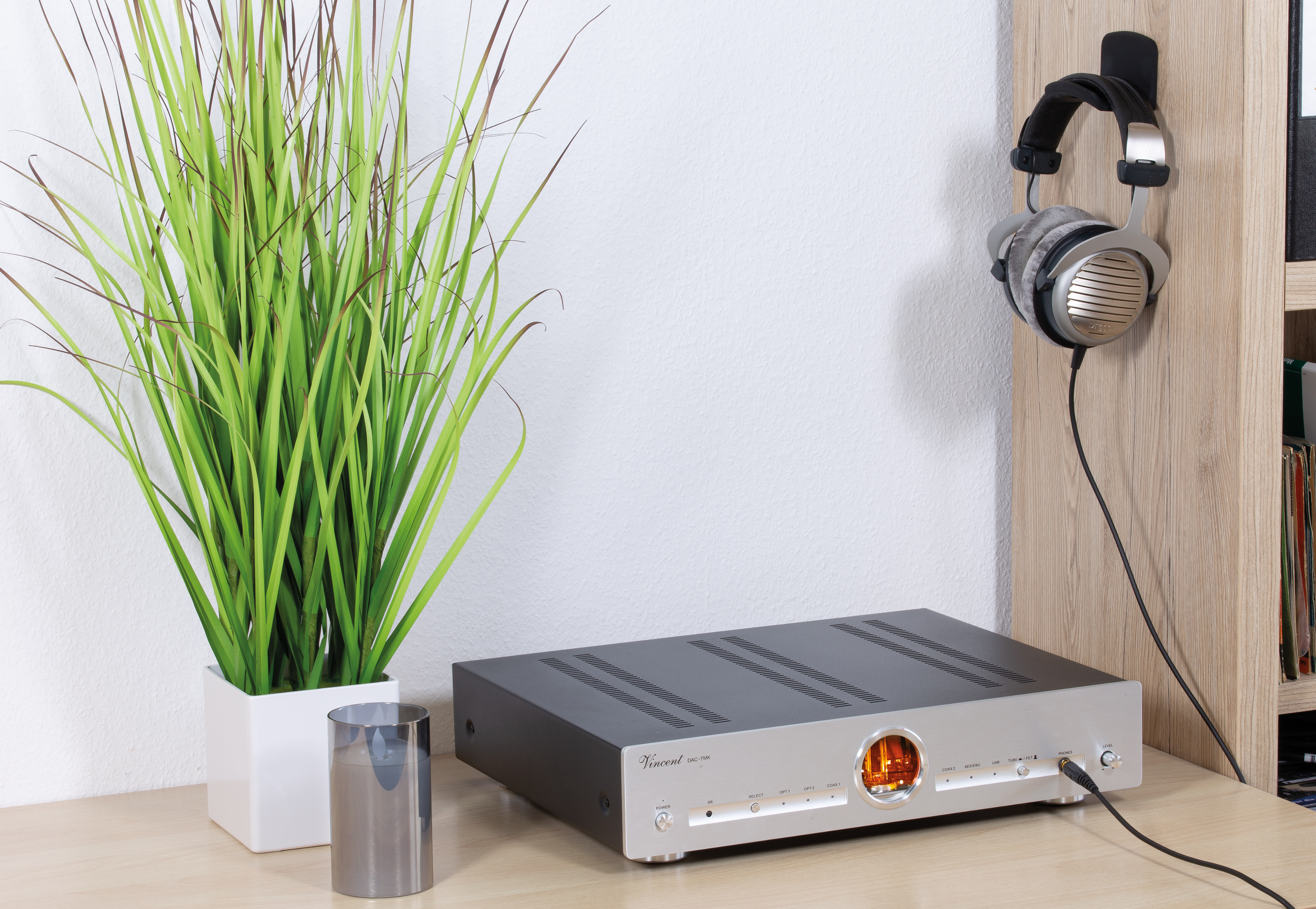 Silberner Audioverstärker mit orangefarbener Anzeige, Kopfhörer auf Holzregal.