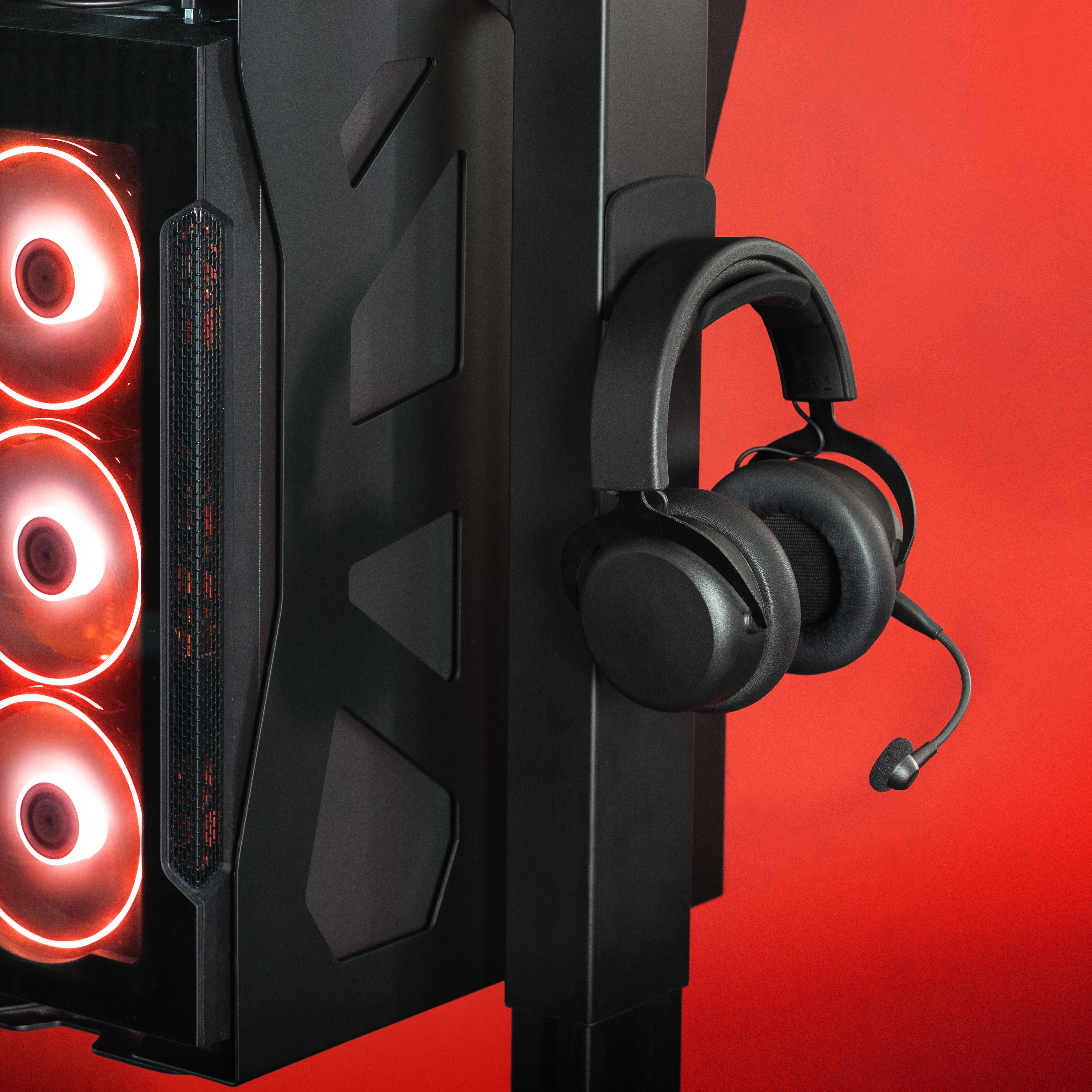 Ein Gaming-PC mit rot beleuchteten Lüftern und einem schwarzen Headset, das an einem Ständer hängt. Der Hintergrund ist rot.