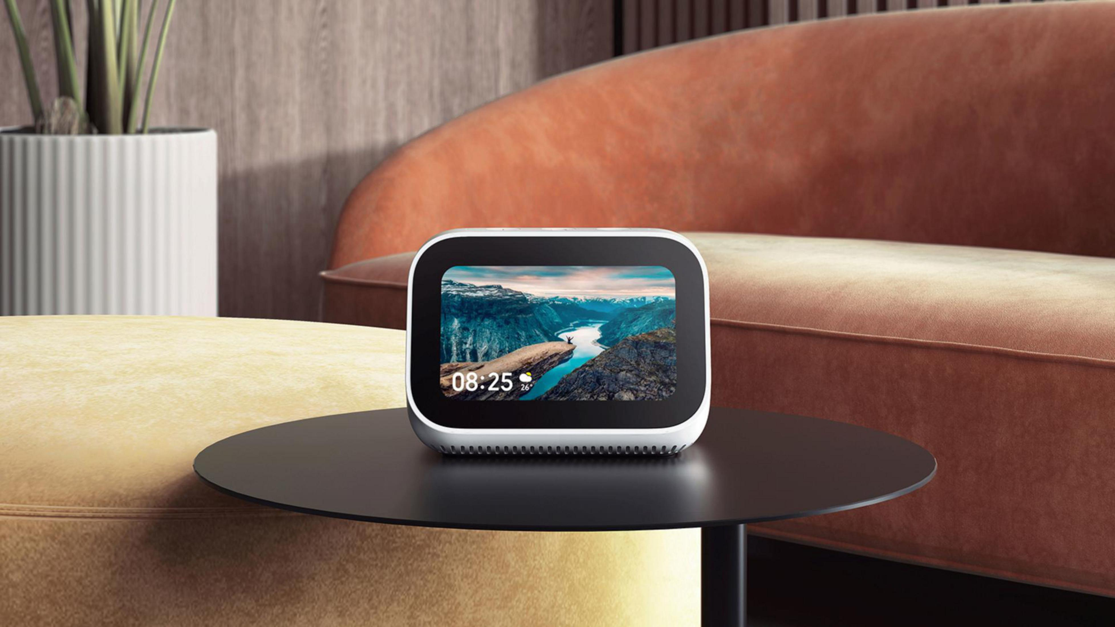 Ein weißes Smart-Display auf einem schwarzen Tisch. Ein Sofa und eine Pflanze sind im Hintergrund.