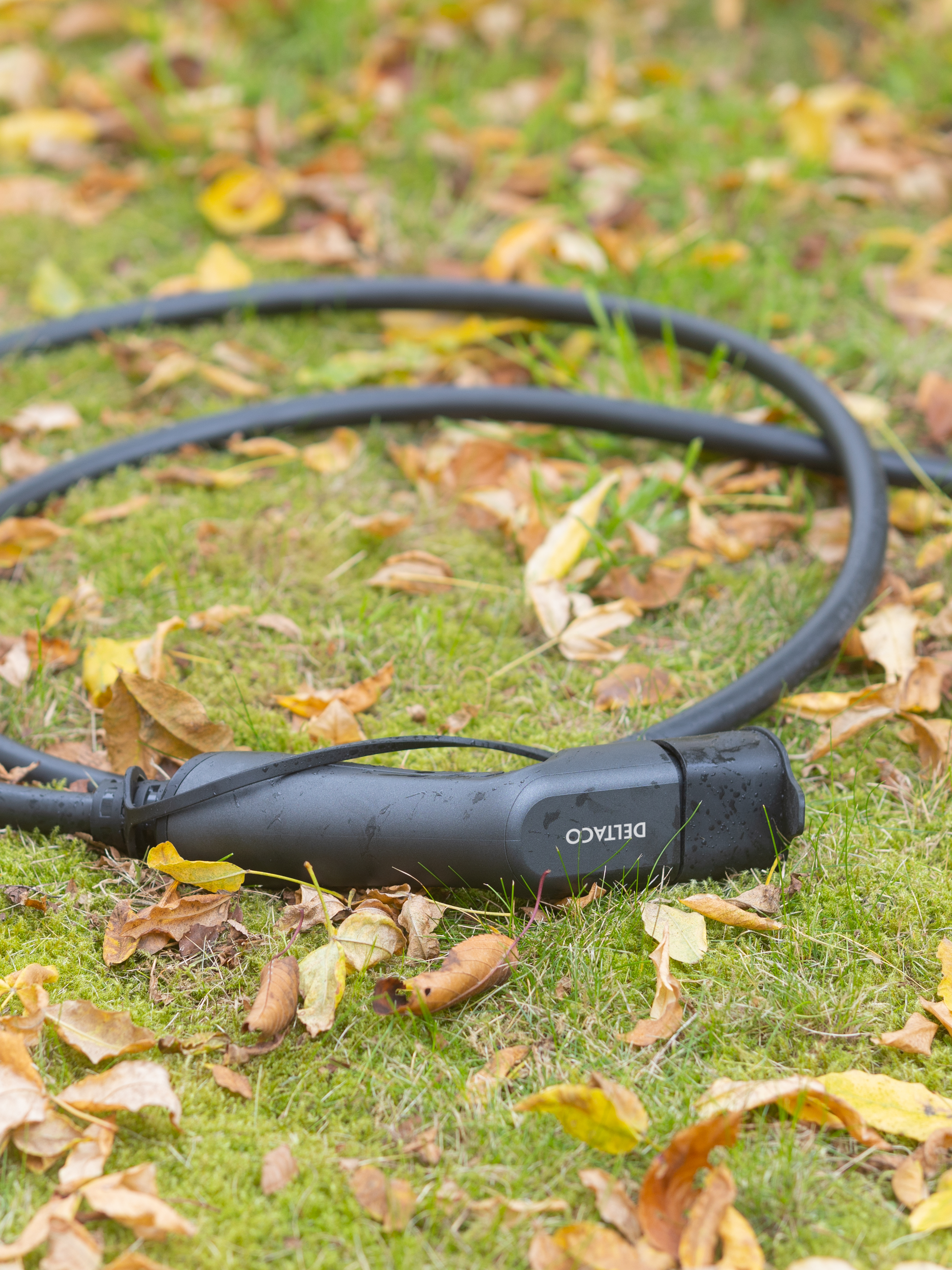Black EV charging cable on grass with fallen leaves. The connector is visible.