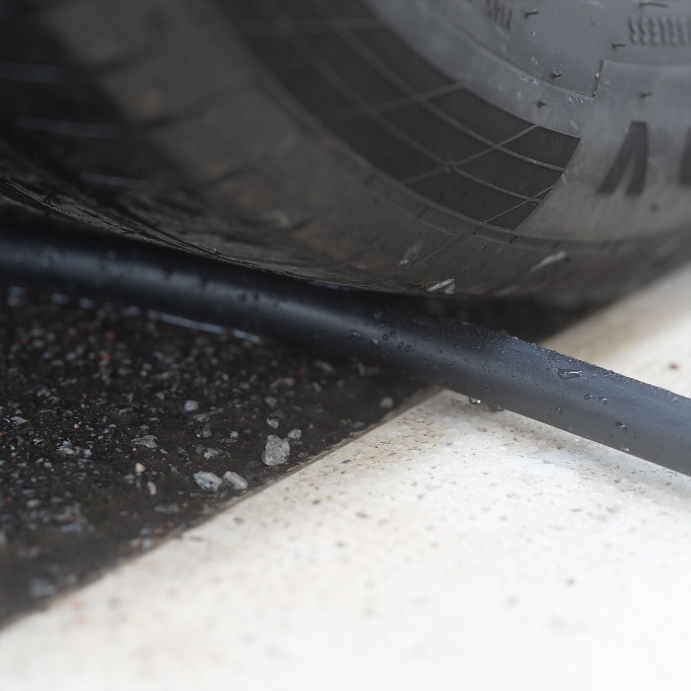Black rubber hose under a tire, on asphalt and concrete. Close-up view.
