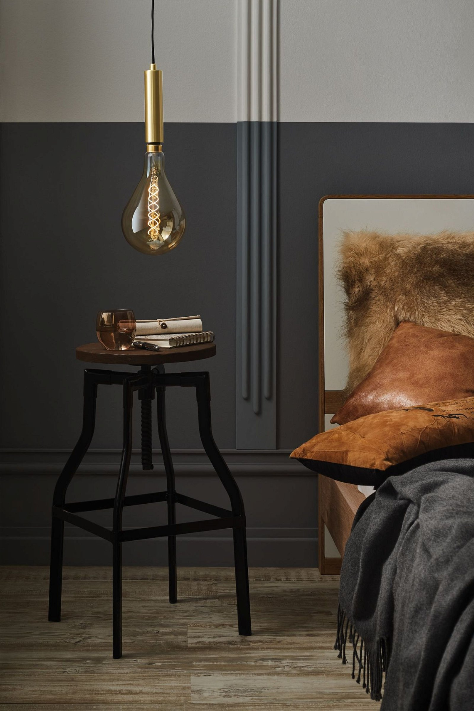 Innenszene mit leuchtender Glühbirne, Hocker, Büchern und einem Bett mit Kissen. Dunkle und neutrale Farben.