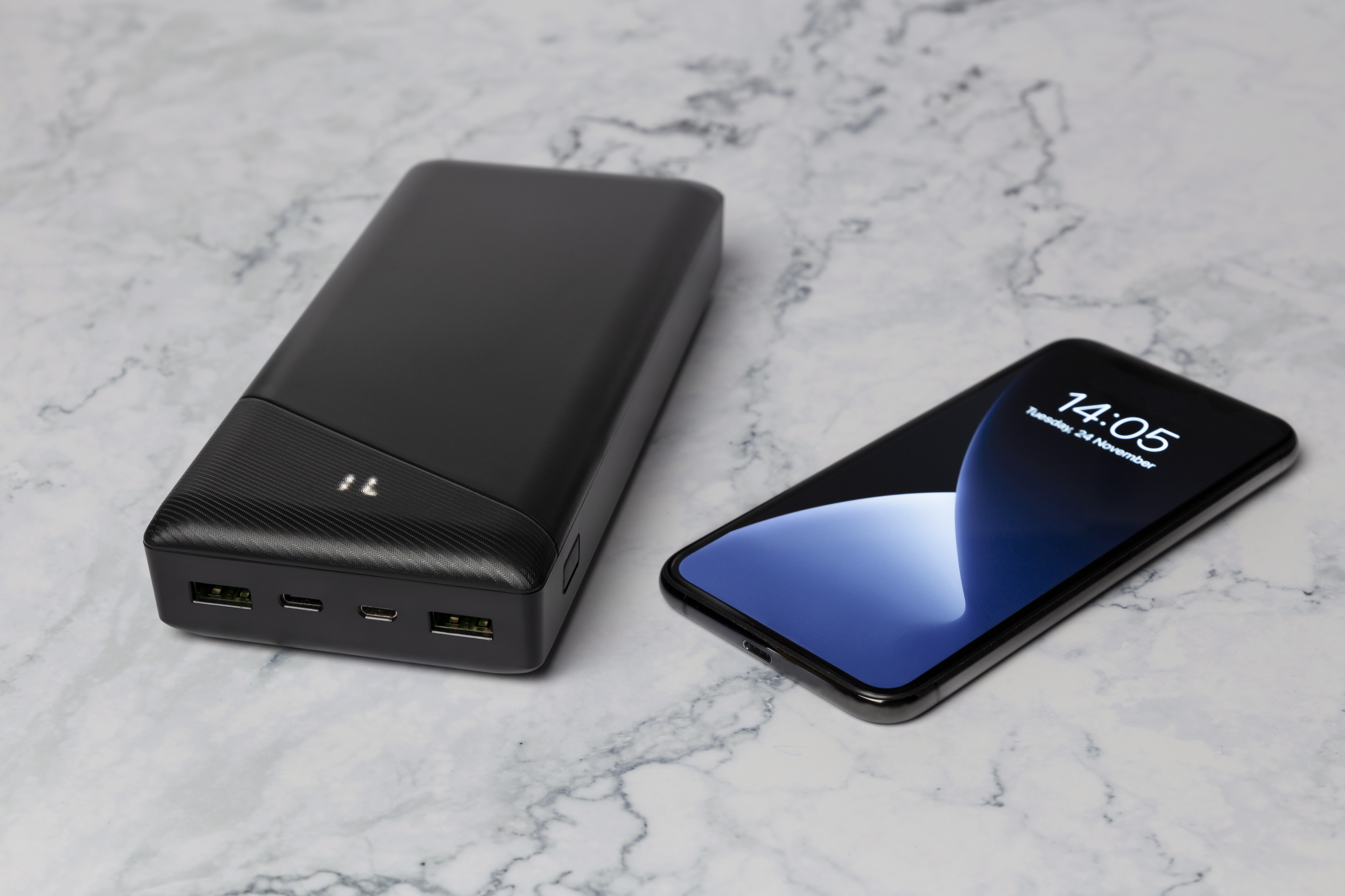 Schwarze Powerbank neben einem Telefon mit 14:05 auf dem Bildschirm.