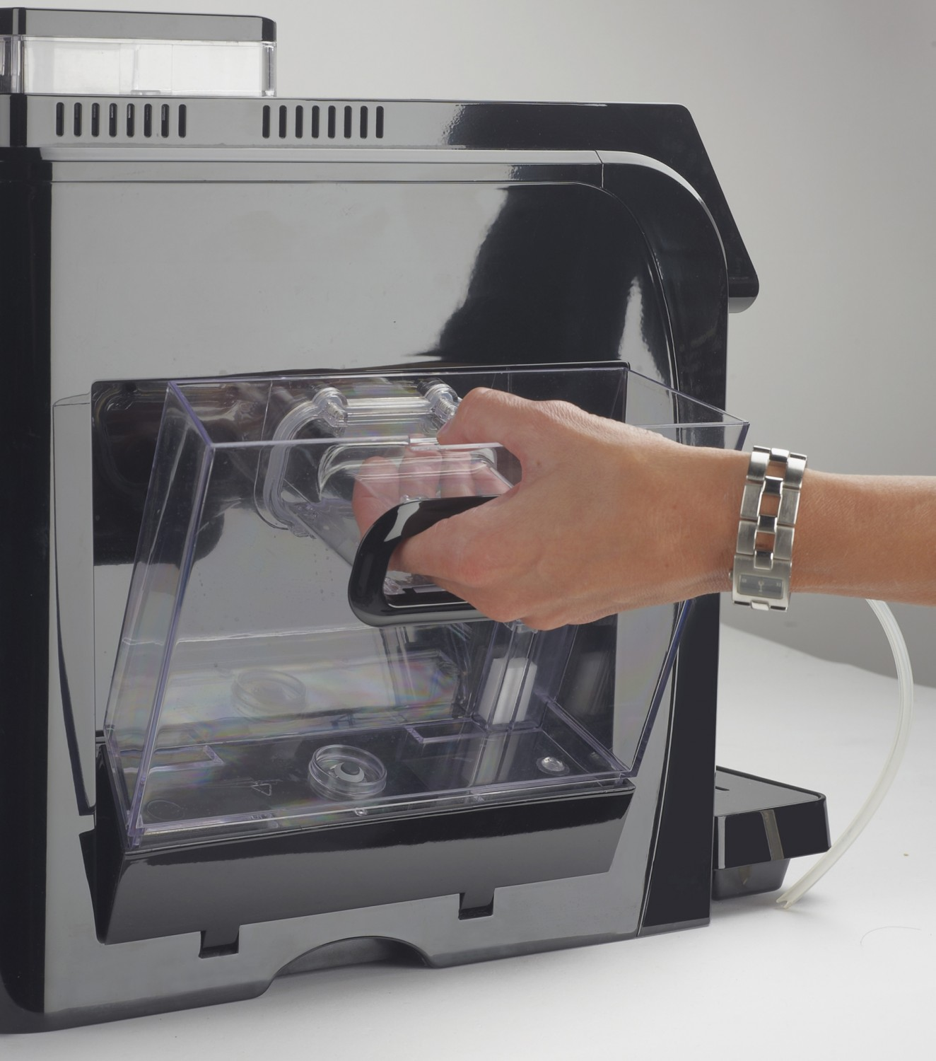 Ręka osoby wyjmuje zbiornik na wodę z czarnego ekspresu do kawy na białym tle.